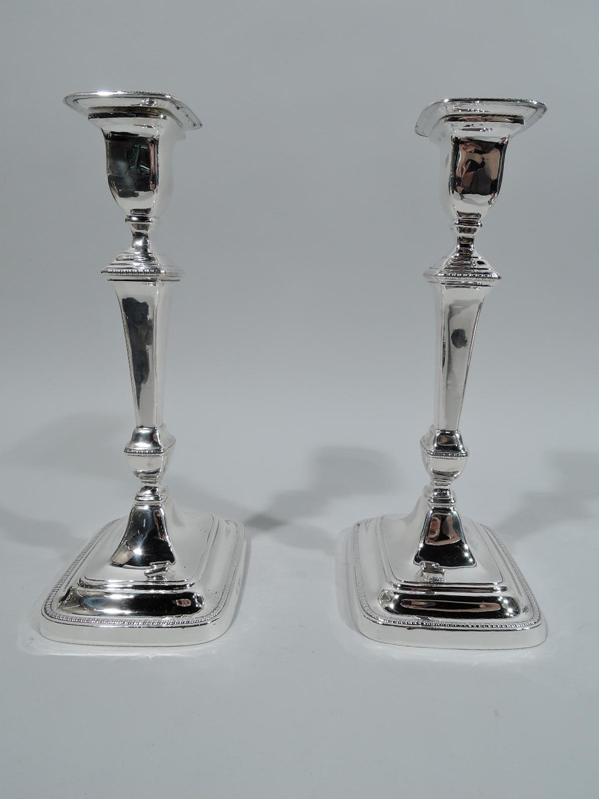 George V sterling silver candlesticks. Made by John Round & Son, Ltd in Sheffield in 1911. Each: Rectilinear with tapering pillar shaft on knop on stepped foot with curved corners. Shaft top stepped with urn socket inset with detachable bobéches.