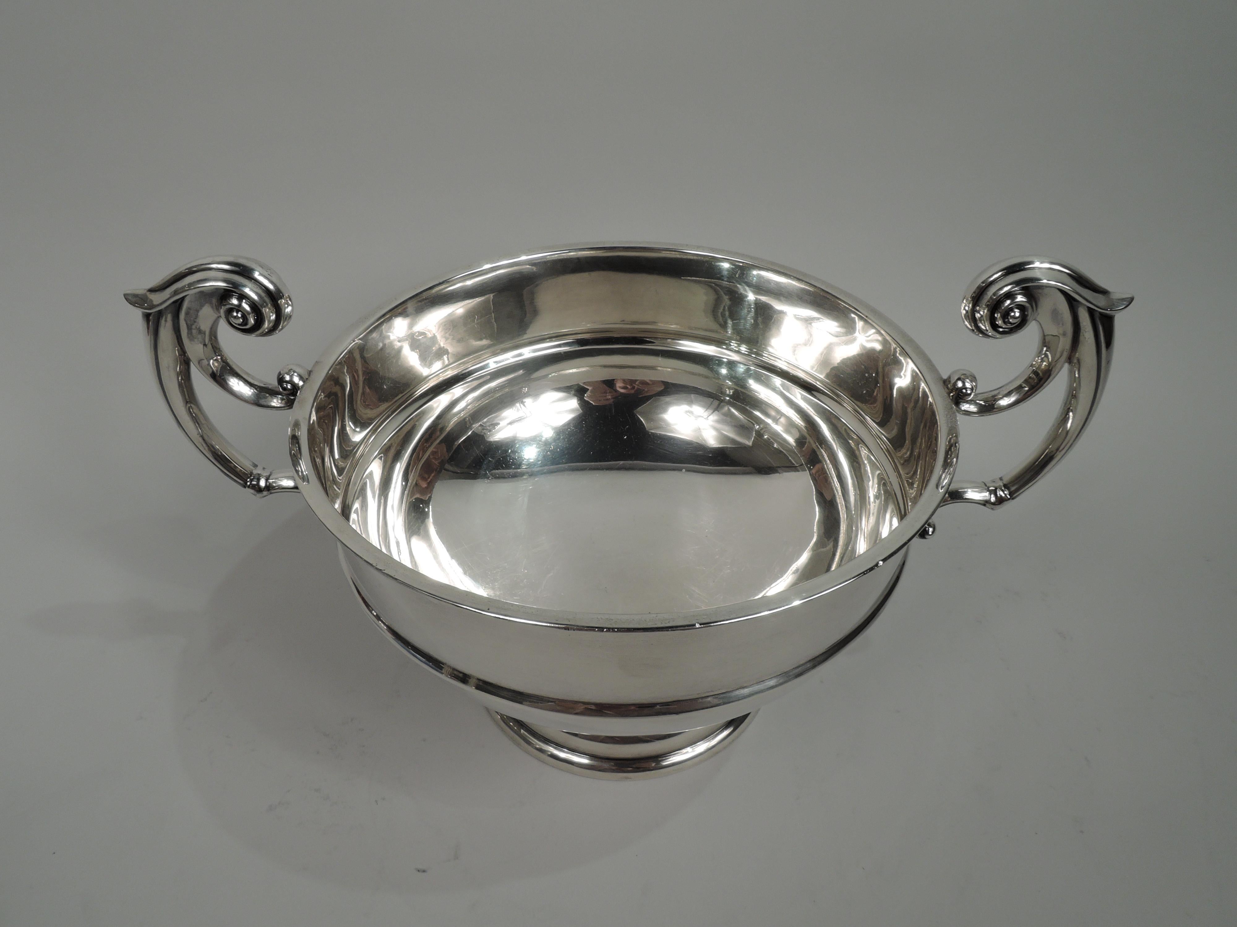 George V sterling silver trophy bowl. Made by John and William Deakin in Sheffield in 1923. Round and girdled with molded rim and curved bottom. Leaf-capped double-scroll flying side handles and domed foot. Traditional Neoclassicism with lots of