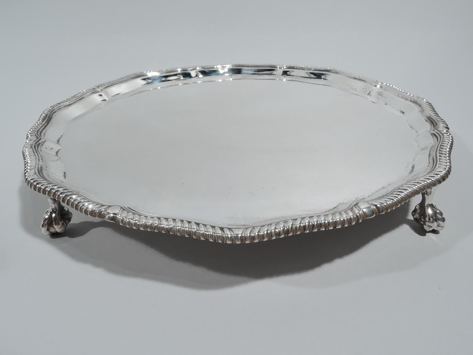 George V sterling silver salver. Made by Thomas Bradbury & Sons in Sheffield in 1921. Round shaped with gently scrolled and gadrooned rim and tapering sides. Four claw-and-ball feet. Traditional Neoclassicism. Fully marked. Weight: 19.5 troy ounces.