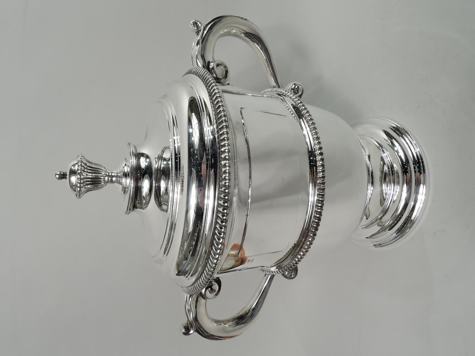 George V sterling silver trophy cup. Made by FC Richards in Birmingham in 1926. Urn with leaf-capped s-scroll side handles, and round and stepped foot. Cover raised with bud finial. Gadrooned rim, girdle, and knop. Traditional Neoclassical form with