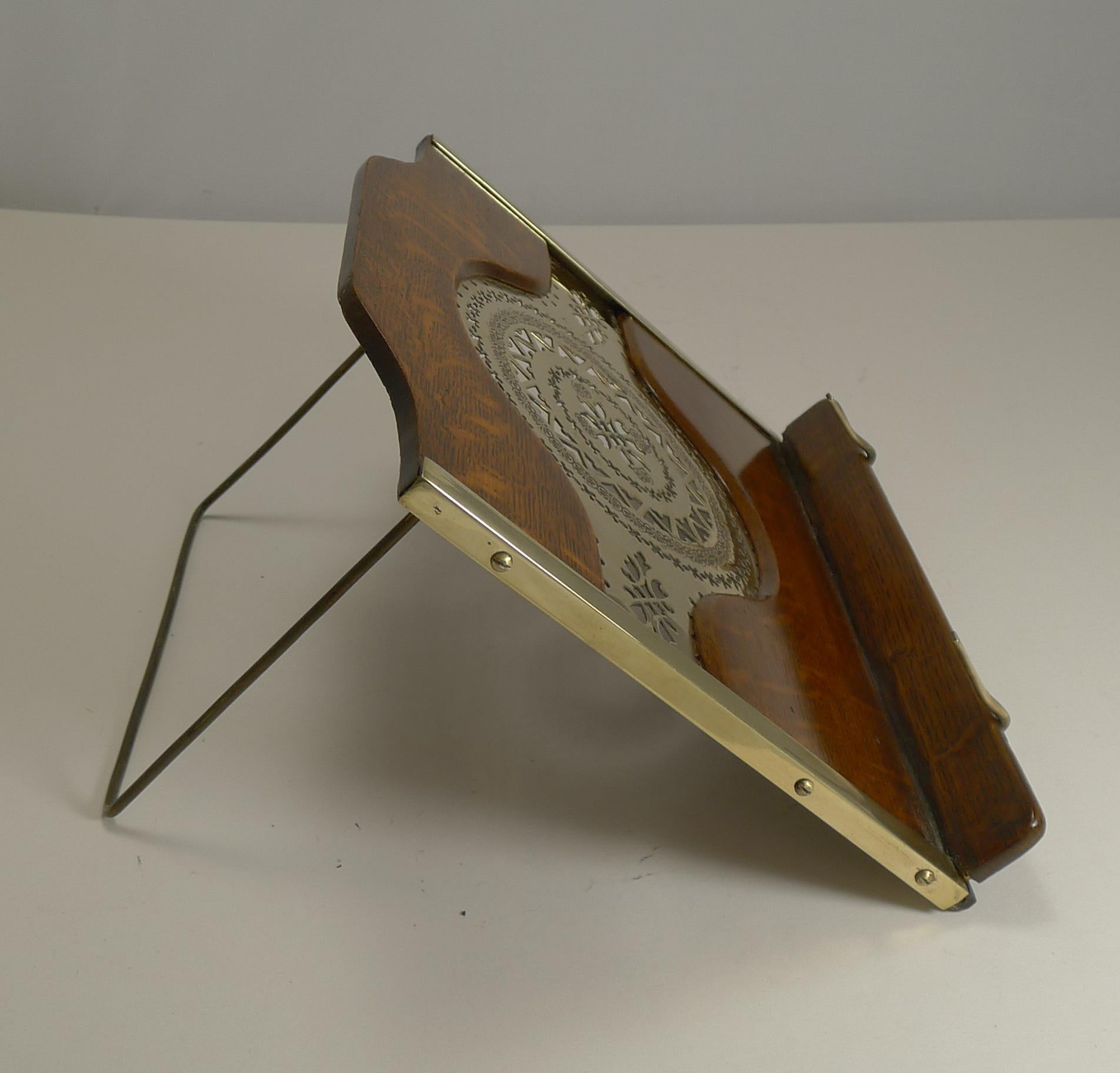 A charming little lectern or book rest made from solid English oak standing on a folding easel back. The sides are trimmed in brass and the oak panels inset with a pierced or reticulated polished brass panel.

The book used for photography