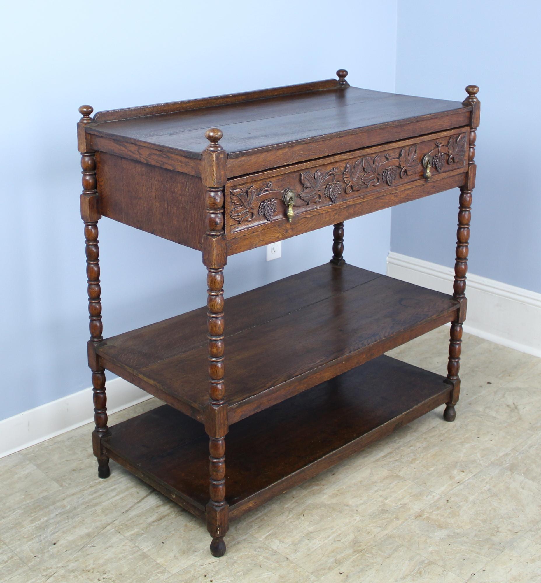 A three-tier dumbwaiter or serving piece with a single large drawer, hand carved with grapes and leaves. The oak has a lovely grain and patina. Height measurement is for total height of the piece.