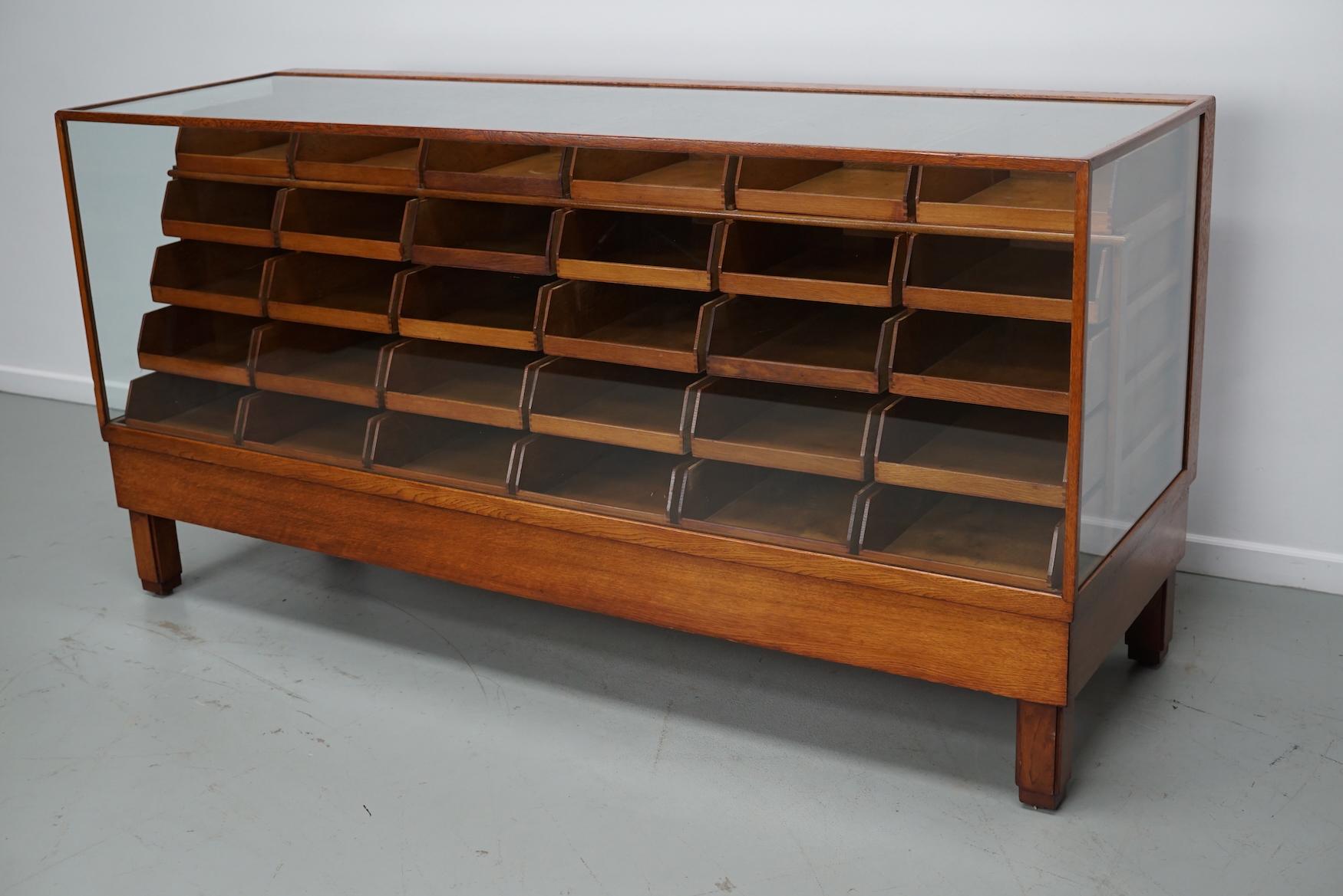 Dieser Kurzwarenladentisch aus Eiche stammt aus den 1920-1930er Jahren und wurde in England hergestellt. Es besteht aus einem massiven Holzrahmen, einem Glasgehäuse mit vielen Schubladen aus Eiche und Griffen aus Eiche.