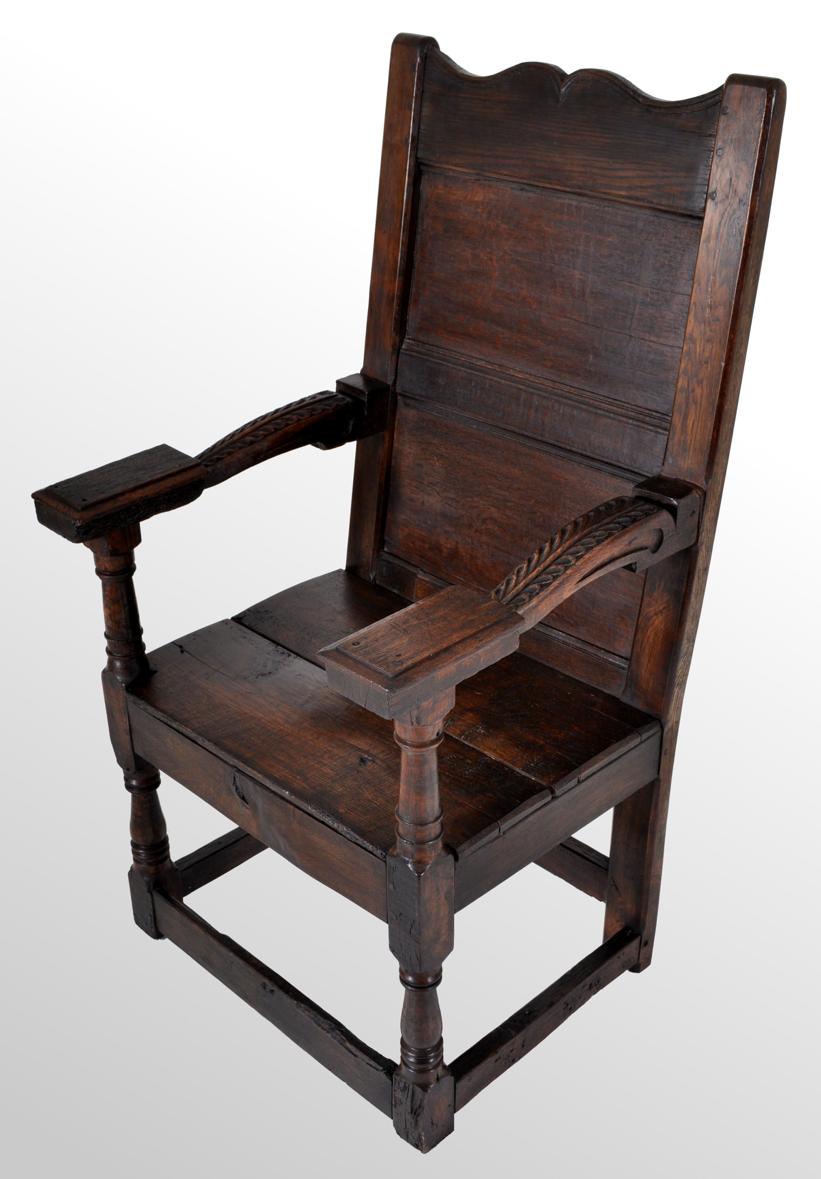 The chair of joined & pegged construction, having a shaped & paneled back, the arms carved & having turned supports. The chair having a simple planked seat and raised of turned legs, the chair having a stretcher on each side. The chair unusually has