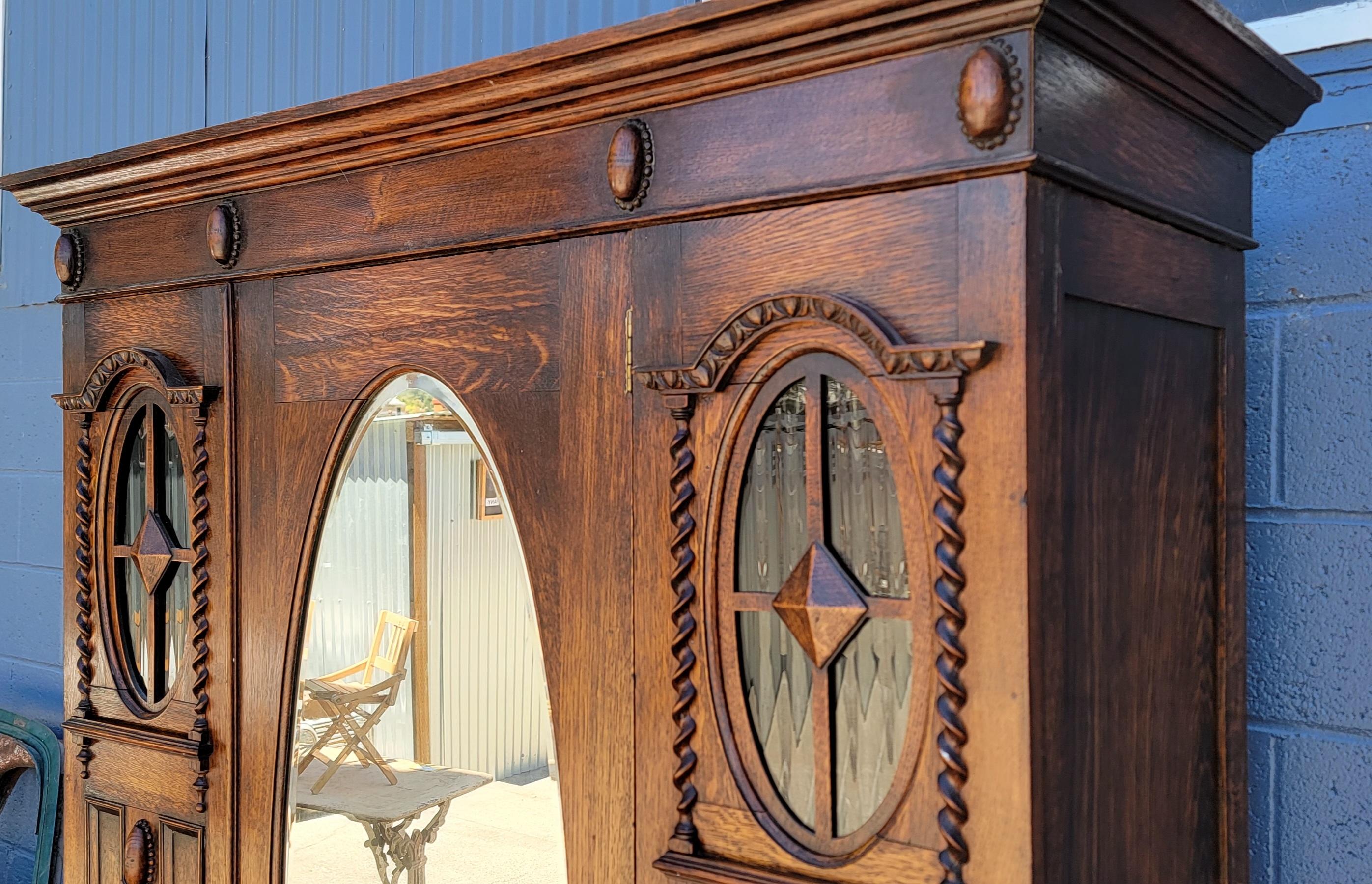 Fine example of a 1930's English tiger oak Jacobean style wardrobe. Exceptional glow to original finish. Original hardware working as in tended. Original oval beveled mirror and ribbed oval glass panels. Original interior brass hanging rod and