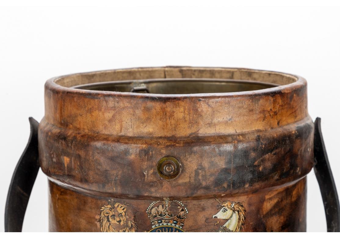 The Bucket is worn overall in keeping with its function. A round leather covered bucket with black leather strap and painted British royal crest. With a removable brass liner. 
Diam. 14 1/2