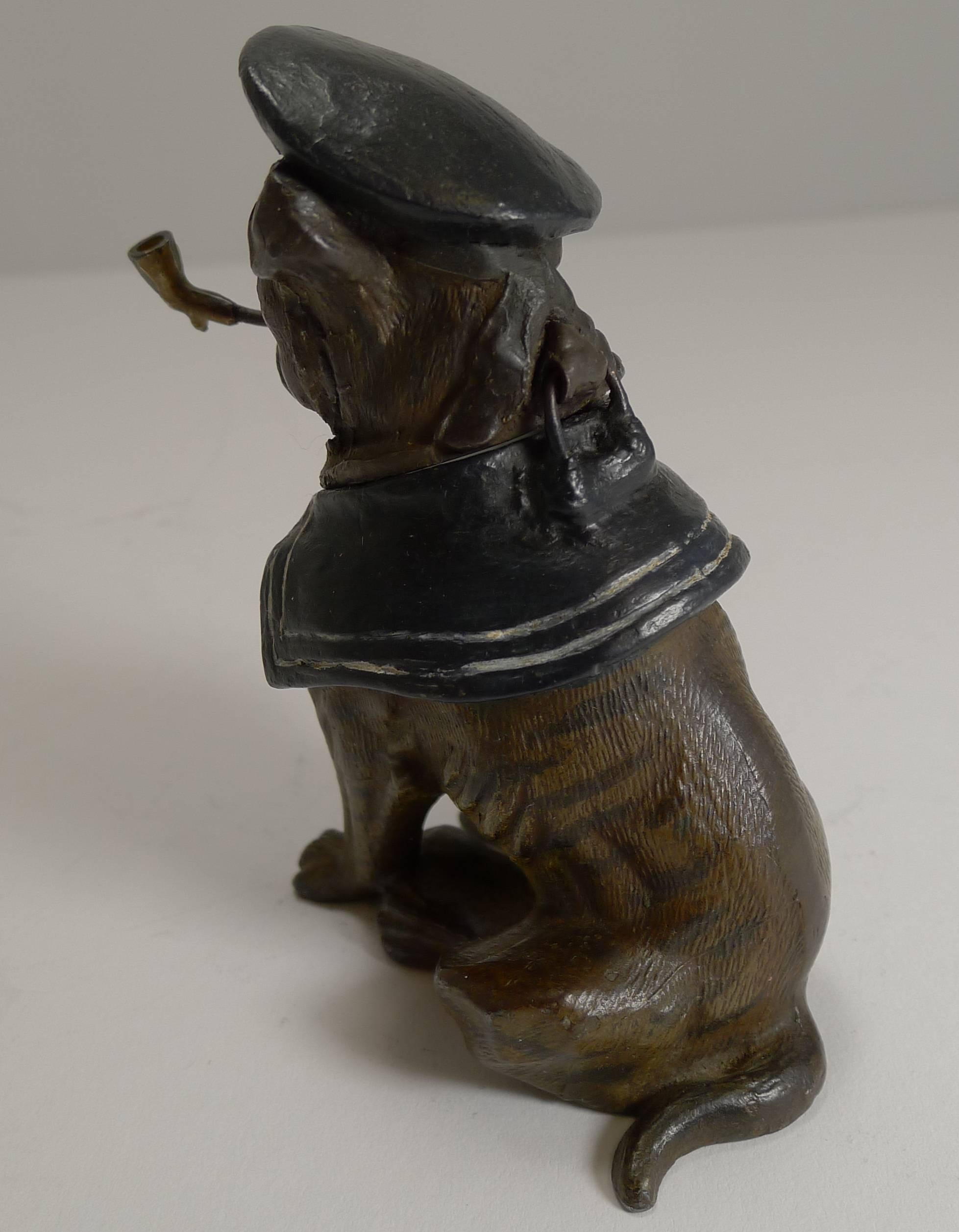 A handsome and very unusual figural inkwell in the form of a British Bulldog dressed with Sailor's attire including the cap and smoking a pipe.

Made from spelter, it is nicely painted. The lid lifts to reveal the removable ceramic ink chamber