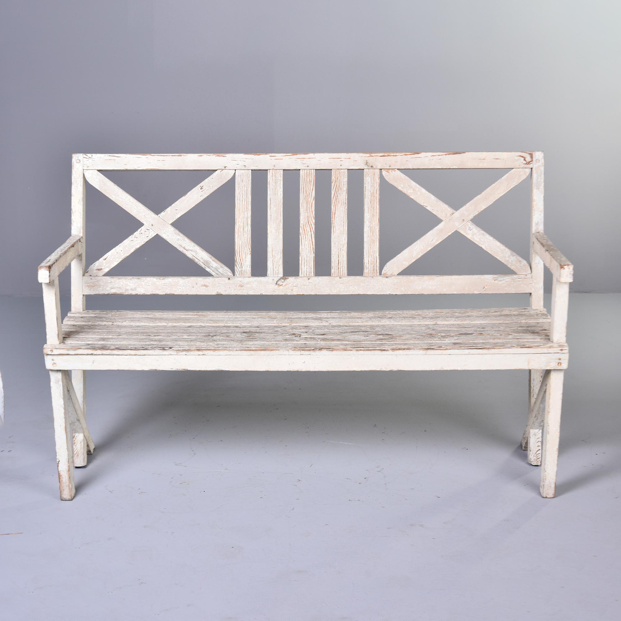 Found in England, this white painted bench dates from the 1920s. Wooden bench has weathered white paint, double X-form seat back, arms and a slatted seat. Unknown maker. 

Arm Height:  28     Seat Height:  18.75
Seat Depth:  16”     Seat Width: 