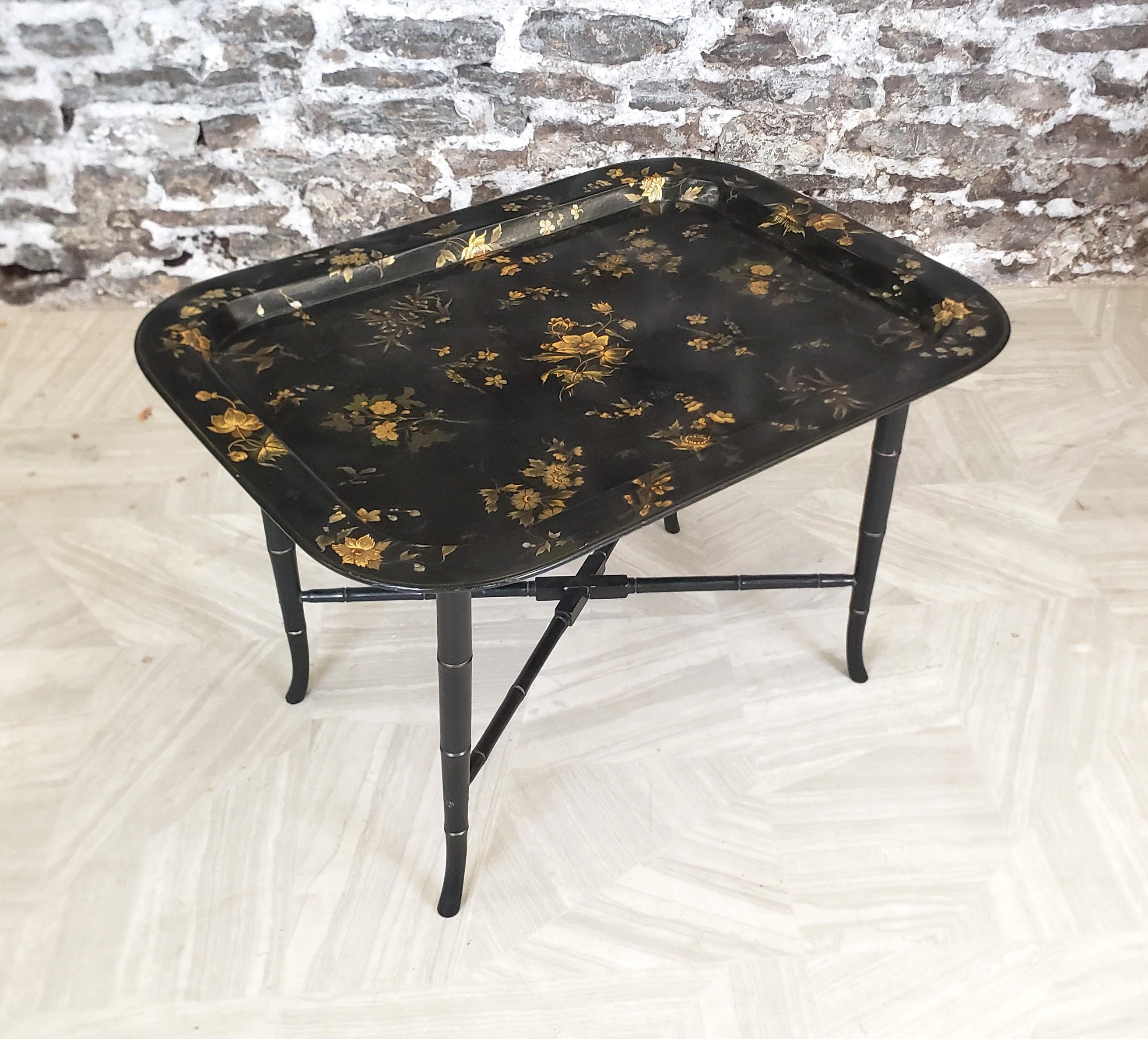 This antique tray table is unsigned, but presumed to have originated from England and date to approximately 1880 and done in a period Victorian style. The antique tray itself is composed of paper mache with ornate gilt floral decoration and a glossy
