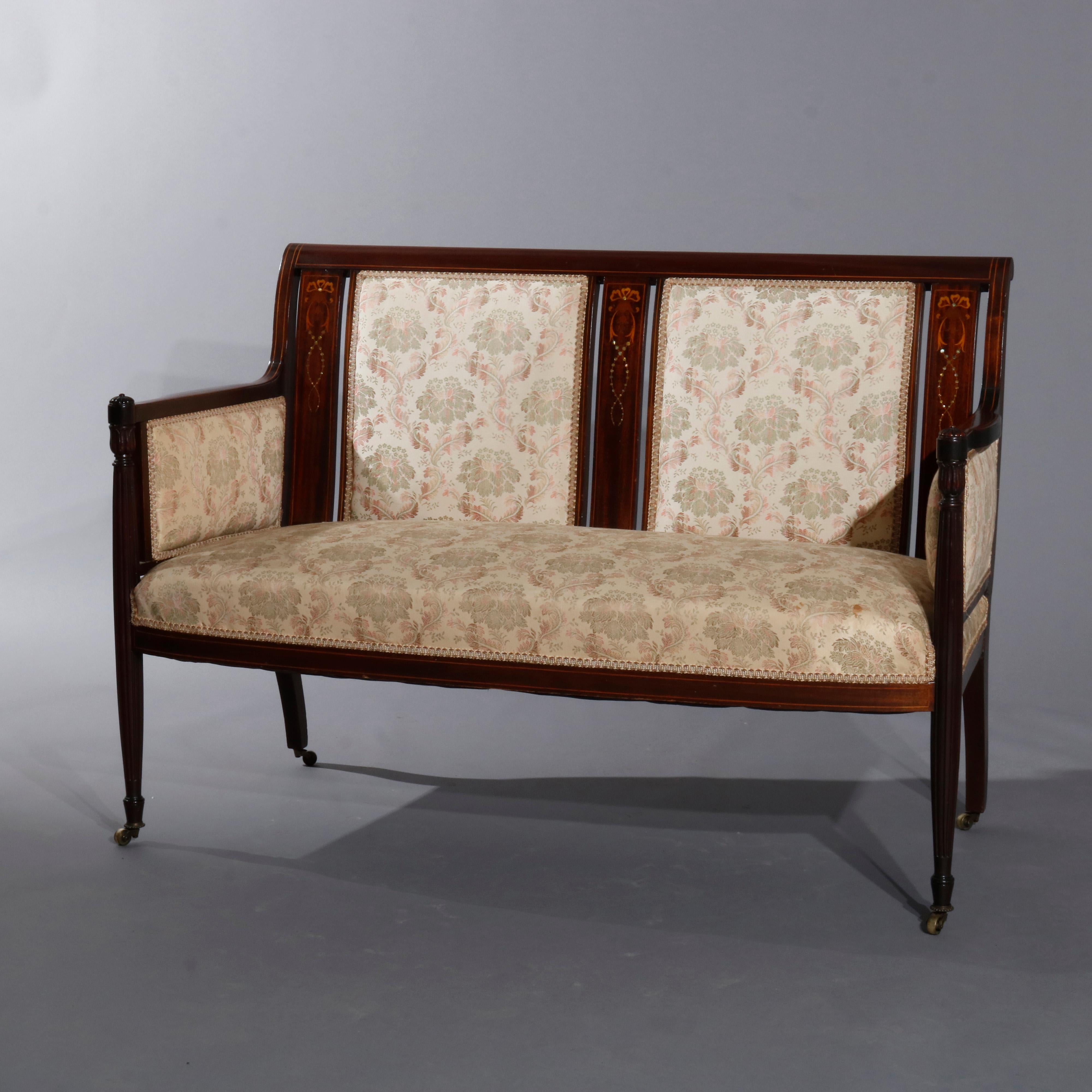 An antique English parlor set includes settle, armchair and side chair offering carved and marquestry mahogany frames with splat back having foliate, scroll and bow satinwood inlay decoration; seats, backs and arms upholstered, circa