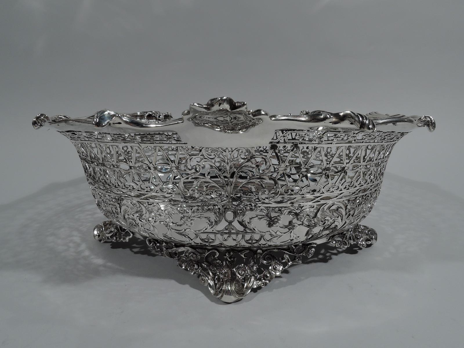 George V sterling silver centerpiece bowl. Made by William Comyns in London in 1911. Oval with solid well and pierced sides. Piercing includes flowers and leaves as well as geometric ornament. Asymmetrical rim has applied scrolls, flowers, and