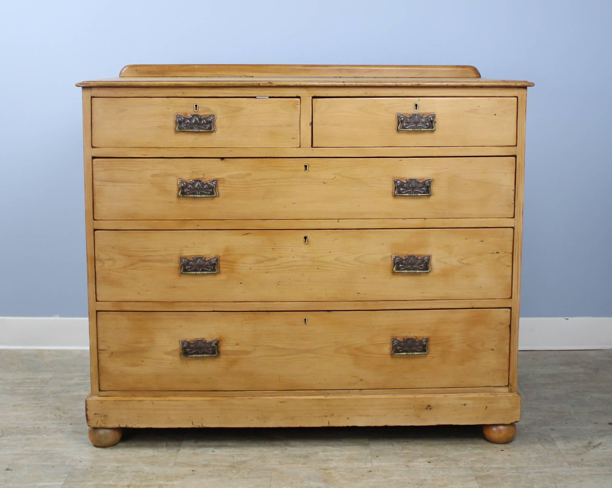 A handsome simple chest of drawers in English Pine. Classic two-over-three configuration with decorative Arts & Crafts brass hardware. The drawers slide easily and are very clean inside. Small gallery on the top adds a decorative note.