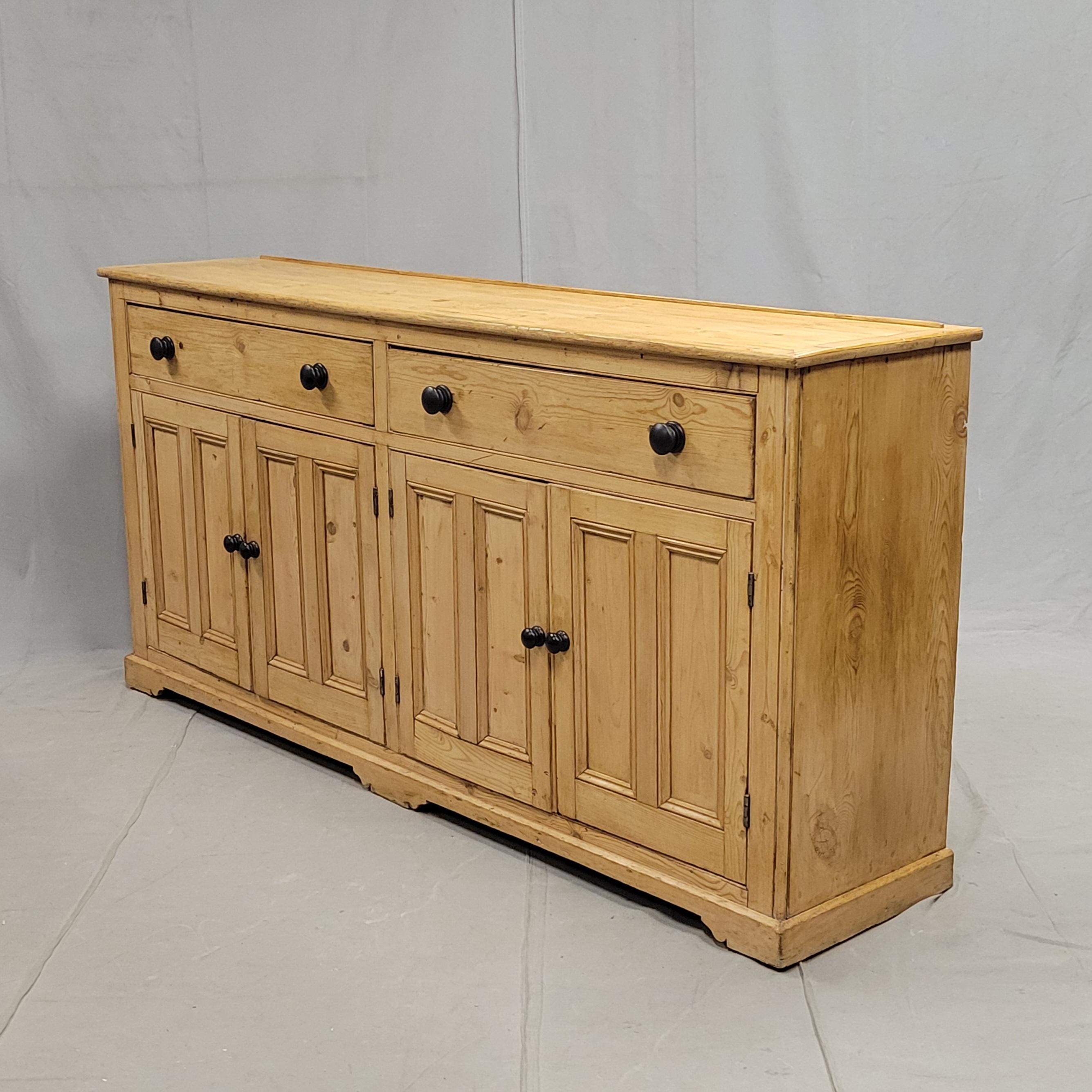 A monumental antique early 20th century English pine sideboard with modern ebonized knobs. The old pine is freshly waxed and buffed to a buttery soft shine. So much storage in this expansive 80