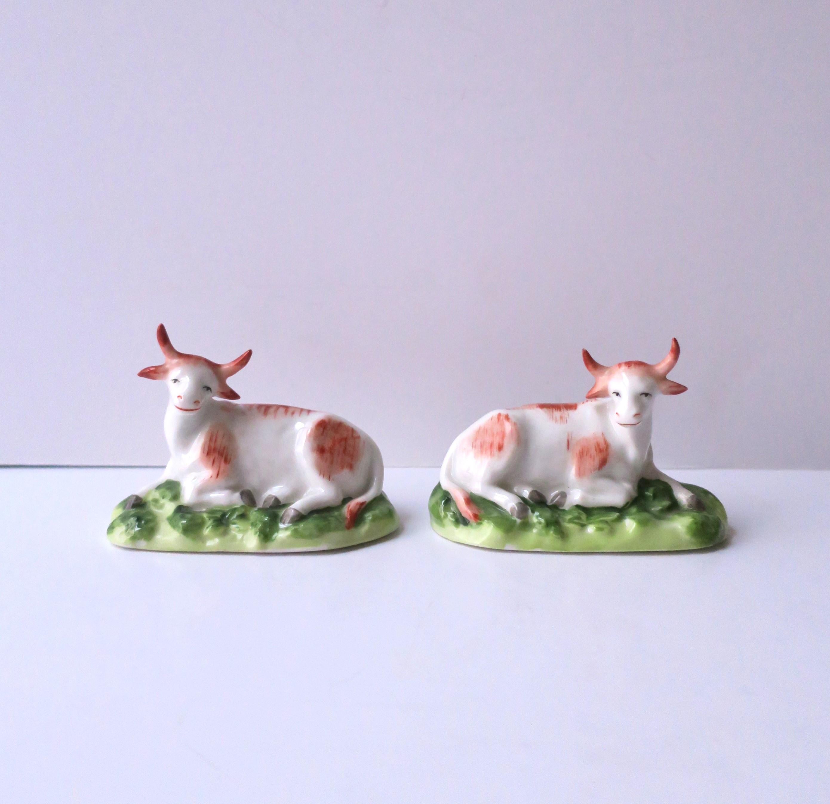 A beautiful and rare pair/set of antique English porcelain hand-painted cows by Chelsea Porcelain company, circa 18th-century, 1756 - 1769, England. Cows/bovine with detailed horns and ears are shown relaxing lying down on green grass pasture, tail
