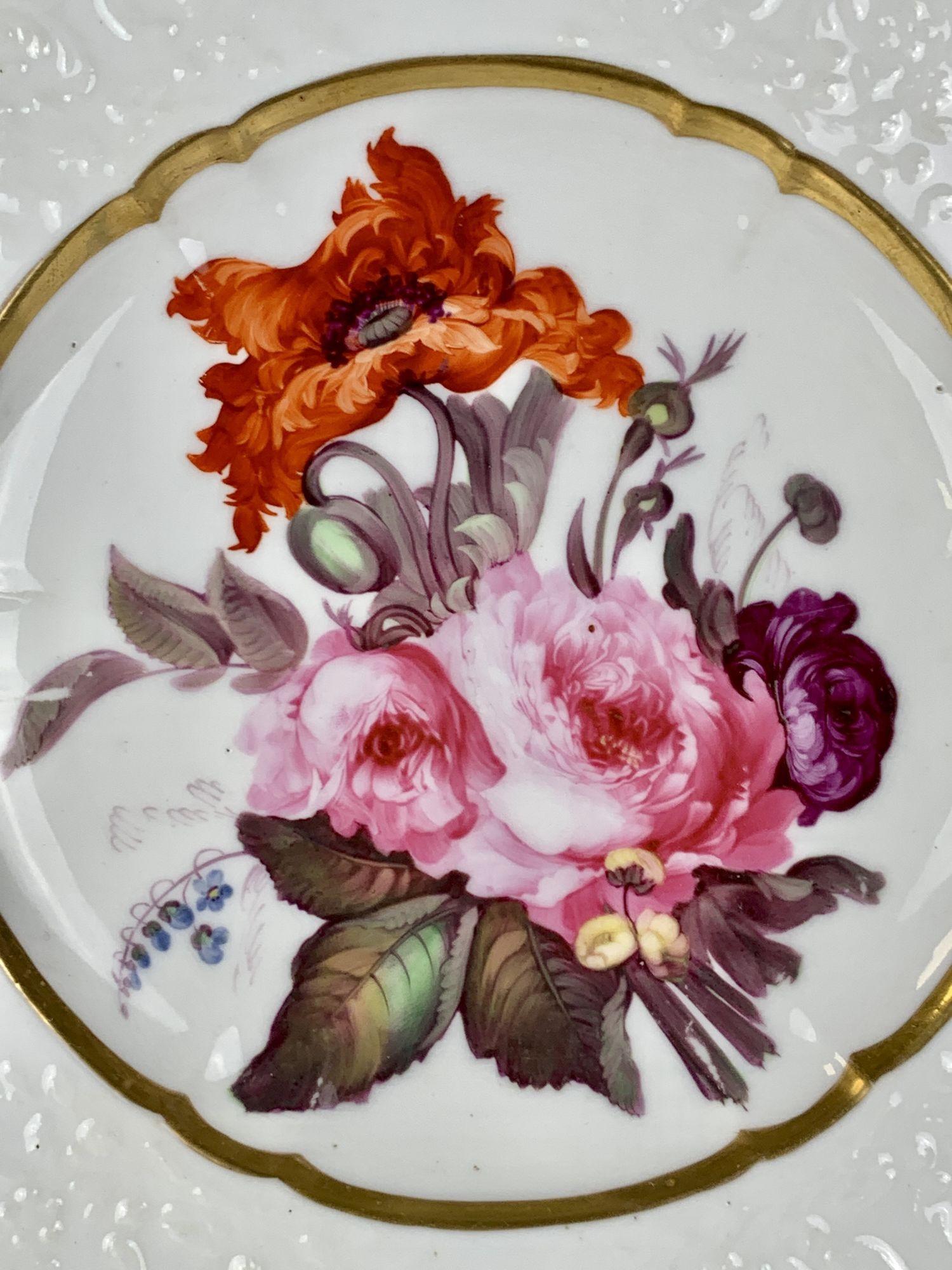 The dish is hand-painted with perfect pink and purple roses and a fabulous orange eastern poppy.
Around the center is a band of gilt. 
The border has impressed decoration of flowers and scrolling vines.
It is an altogether lovely