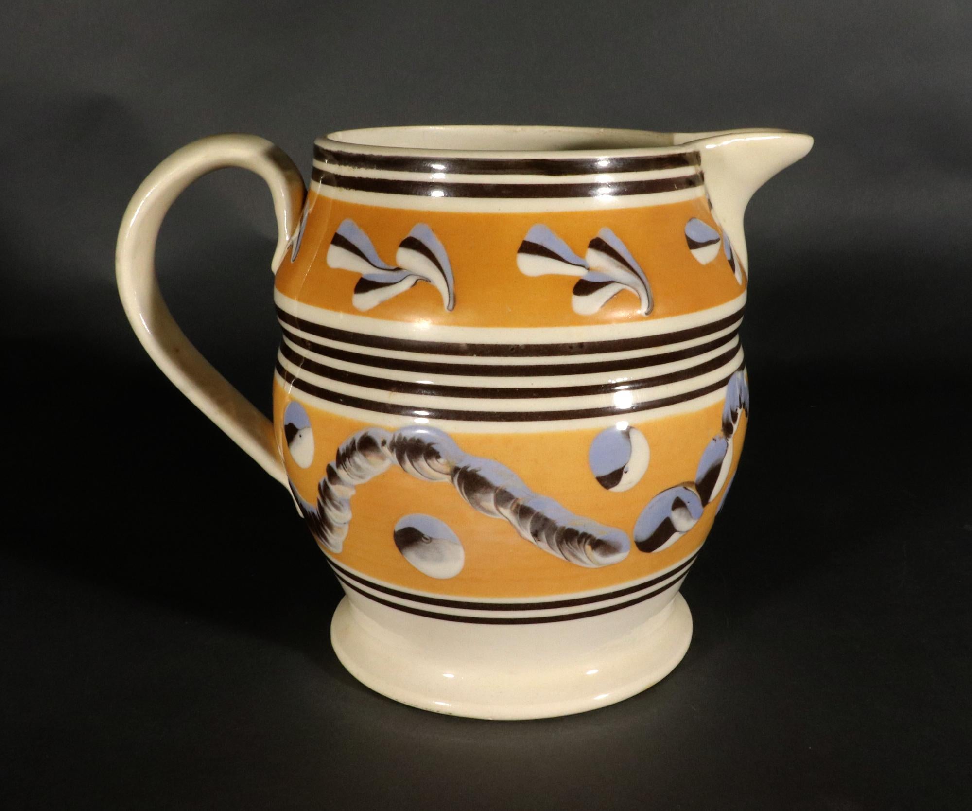 English Pottery Dark Yellow Mocha Jug with Leaf, Earthworm and dot Decoration,
Circa 1800

The jug has a loop handle and pinched spout.  There are two dark yellow bands around the body, the lower one with a tri-color wavy chain band and with