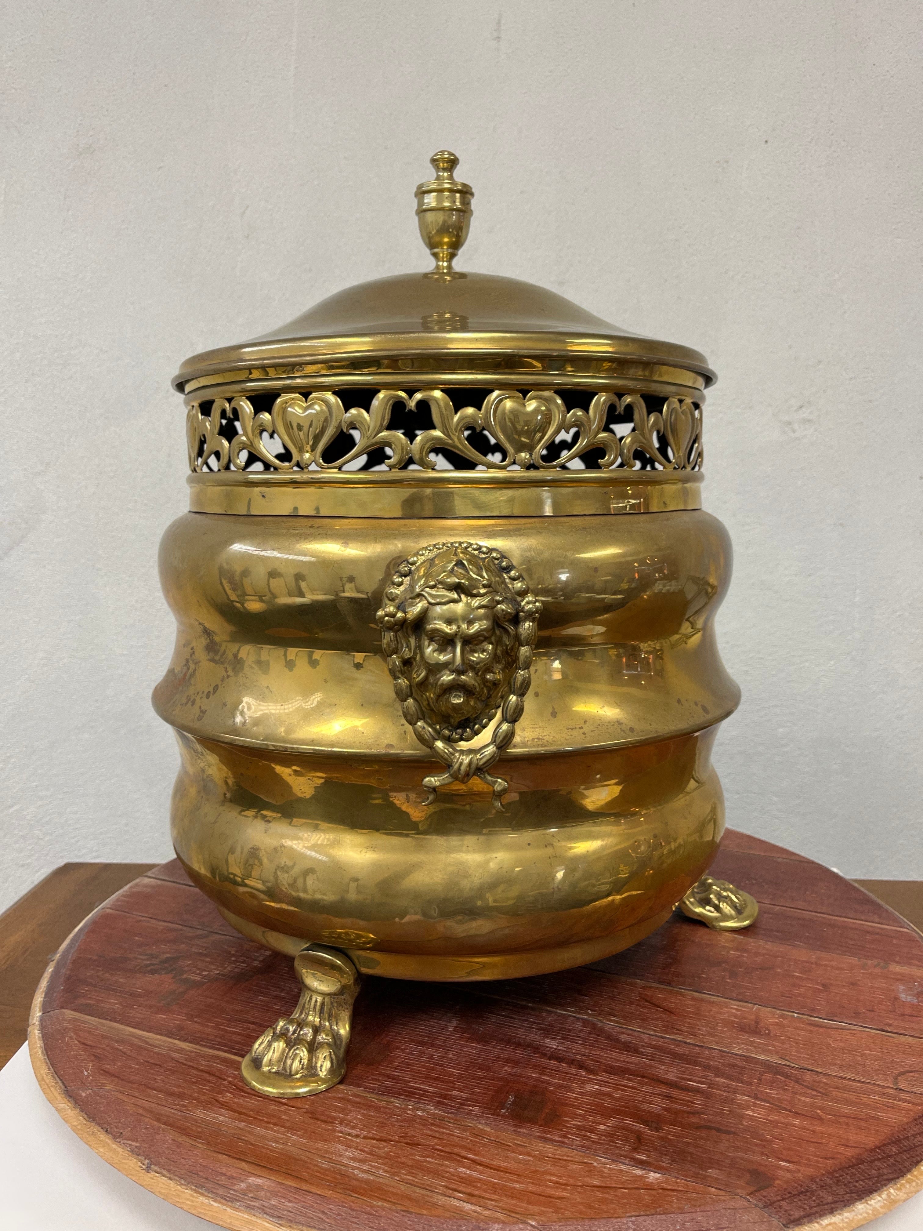 This is a superb example of a brass Regency Purdonium or coal scuttle. The base features highly detailed cast brass figural handles and chiseled articulated lion paw feet. The vessel is surrounded by detailed filigree ventilation. The lid is