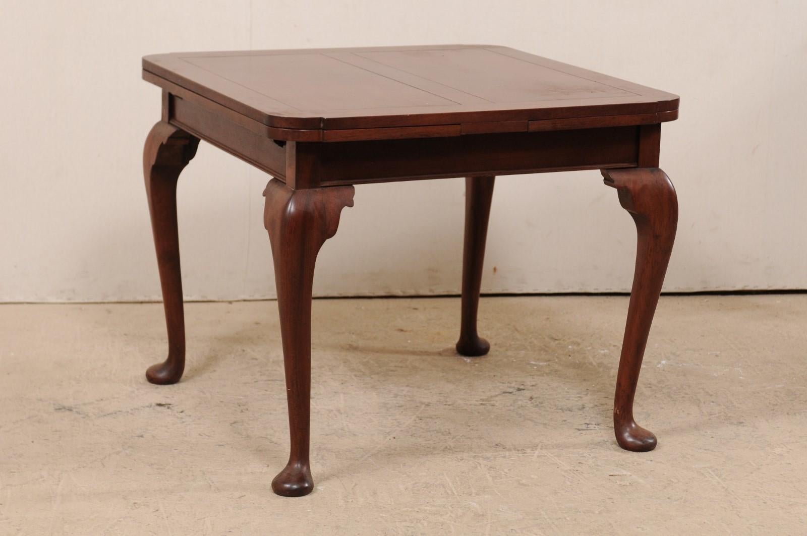 Tavolo Queen Anne inglese dei primi del Novecento, in legno di mogano, sollevato su gambe a cabriole e piedi a pad. Questo tavolo antico di forma quadrata è dotato di due foglie alloggiate sotto il piano che, una volta esteso, permette di regolare