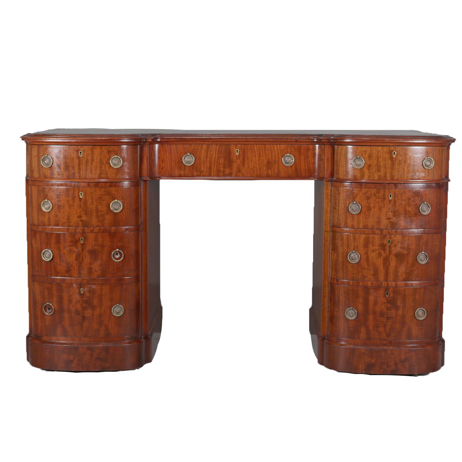 An antique English Regency flame mahogany executive campaign desk featuring knee hole form with gilt decorated leather top writing surface over central drawer with flanking columns each with drawers, cast bronze pulls throughout, circa