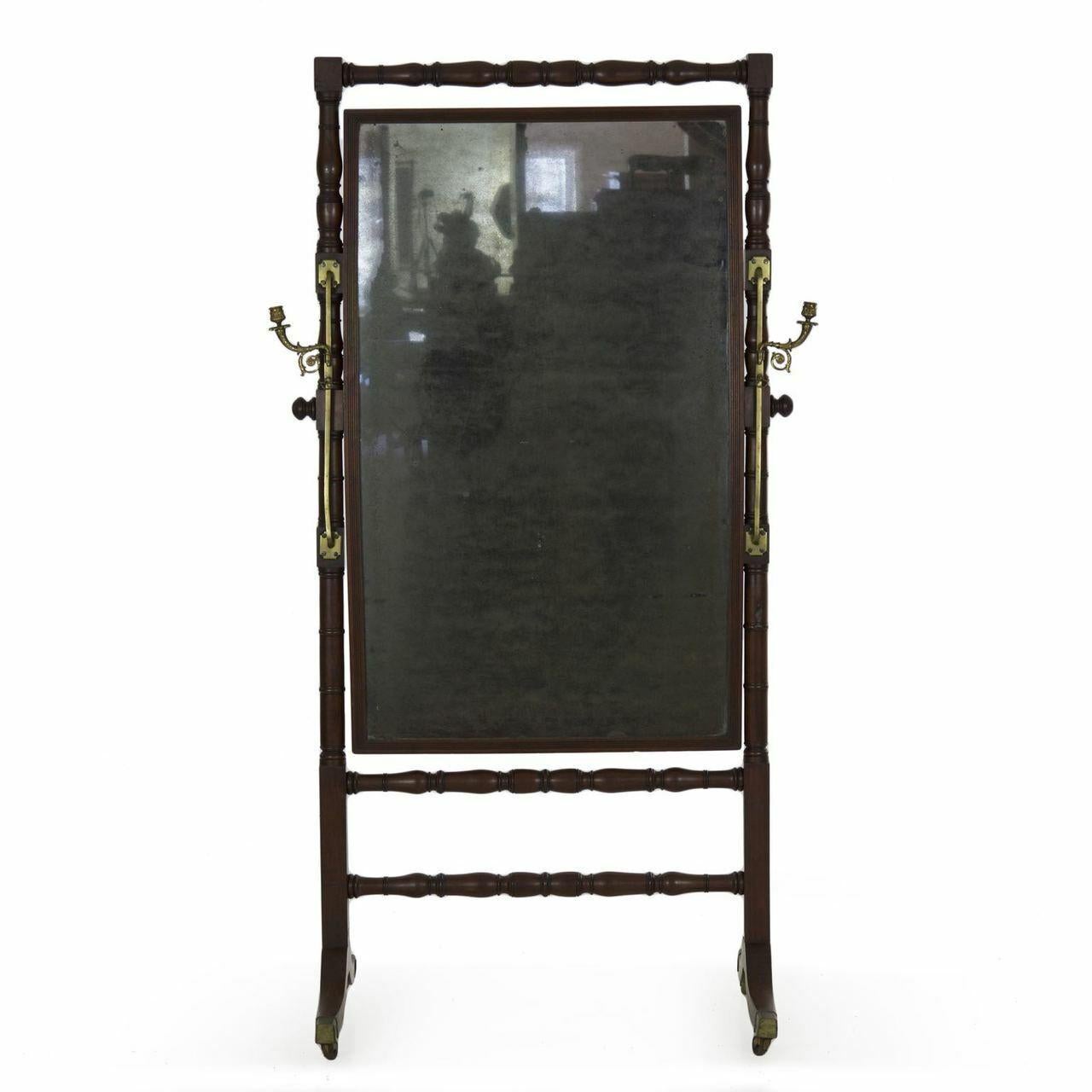 A large and striking cheval mirror from the Regency period, this attractive piece is such an interesting design element with original cast brass hardware and candle sconces and angular form. The turned mahogany frame holds the mahogany box housing