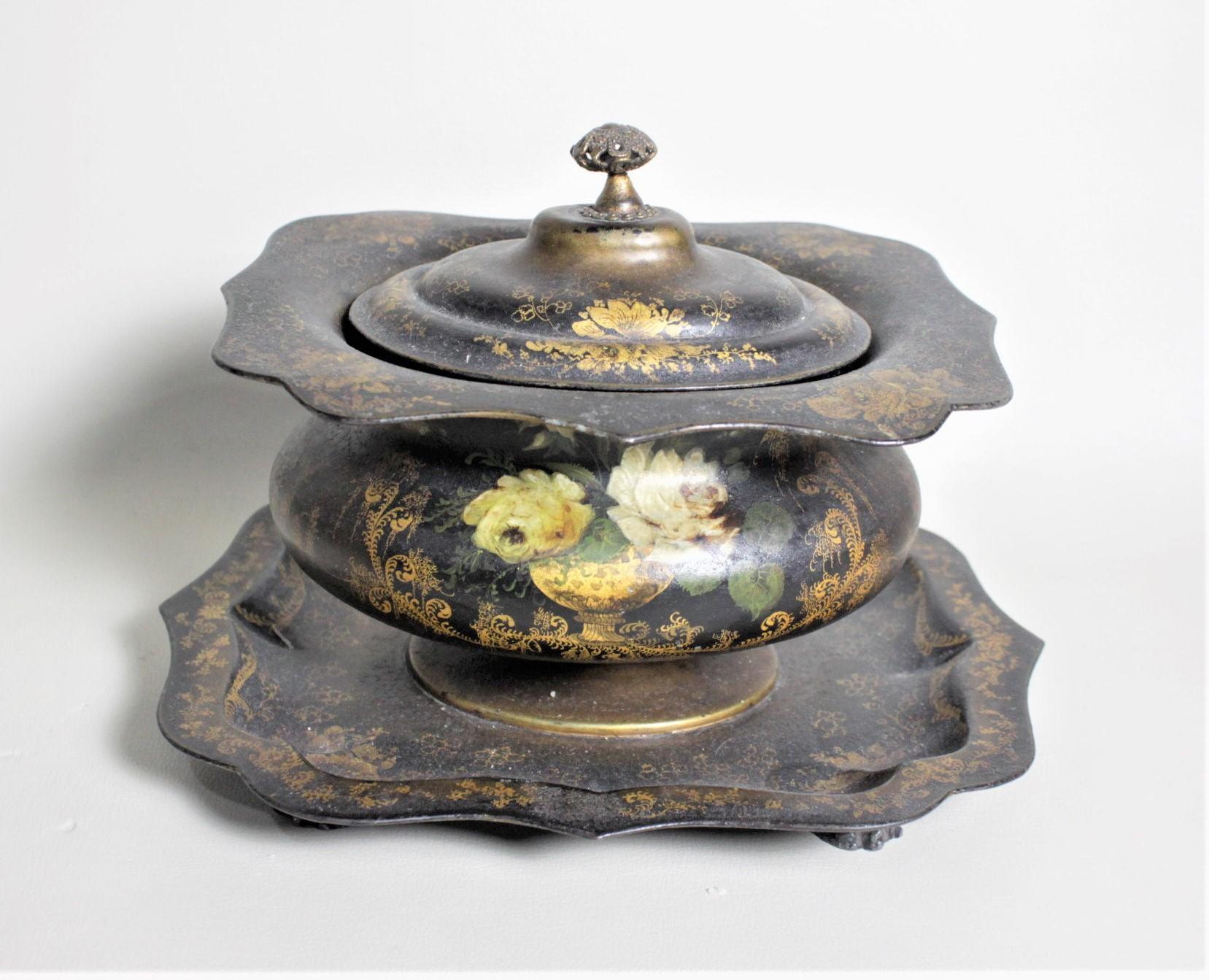 This antique English toleware tea caddy dates to circa 1820 and done in the period Regency style. This tea caddy is constructed of tin with a cast iron handled weight which functions as a manner to compress the tea. The body of the caddy is caldron
