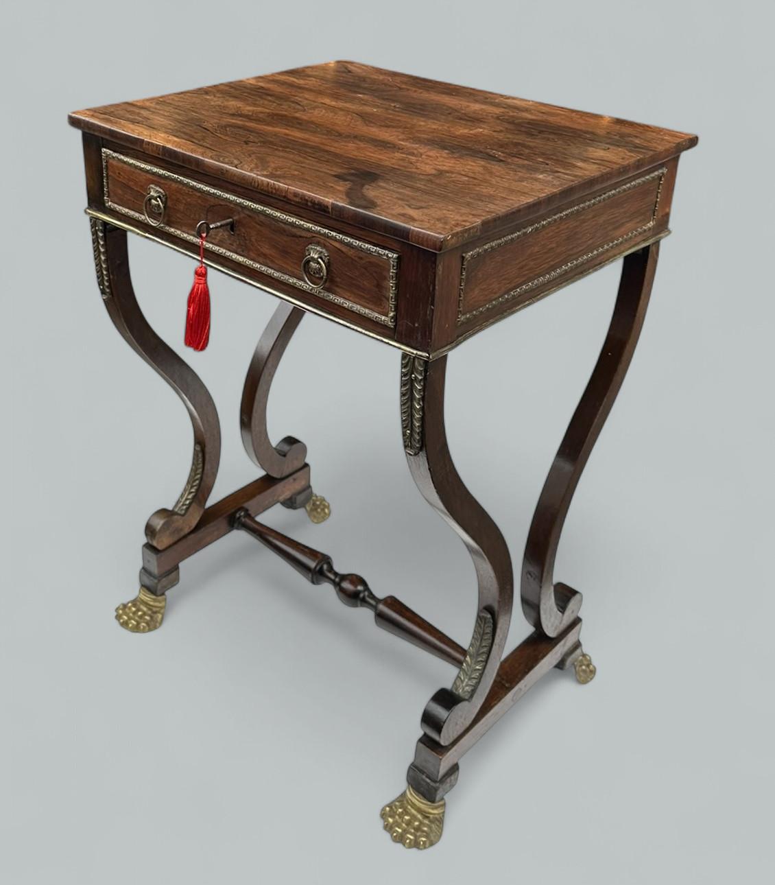Elegante tavolo da centro, laterale o da lavoro inglese in legno di palissandro ben scolpito e metallo dorato di proporzioni compatte, risalente agli inizi del XIX secolo, periodo Regency. 

Il piano d'appoggio rettangolare e figurato è posto al di