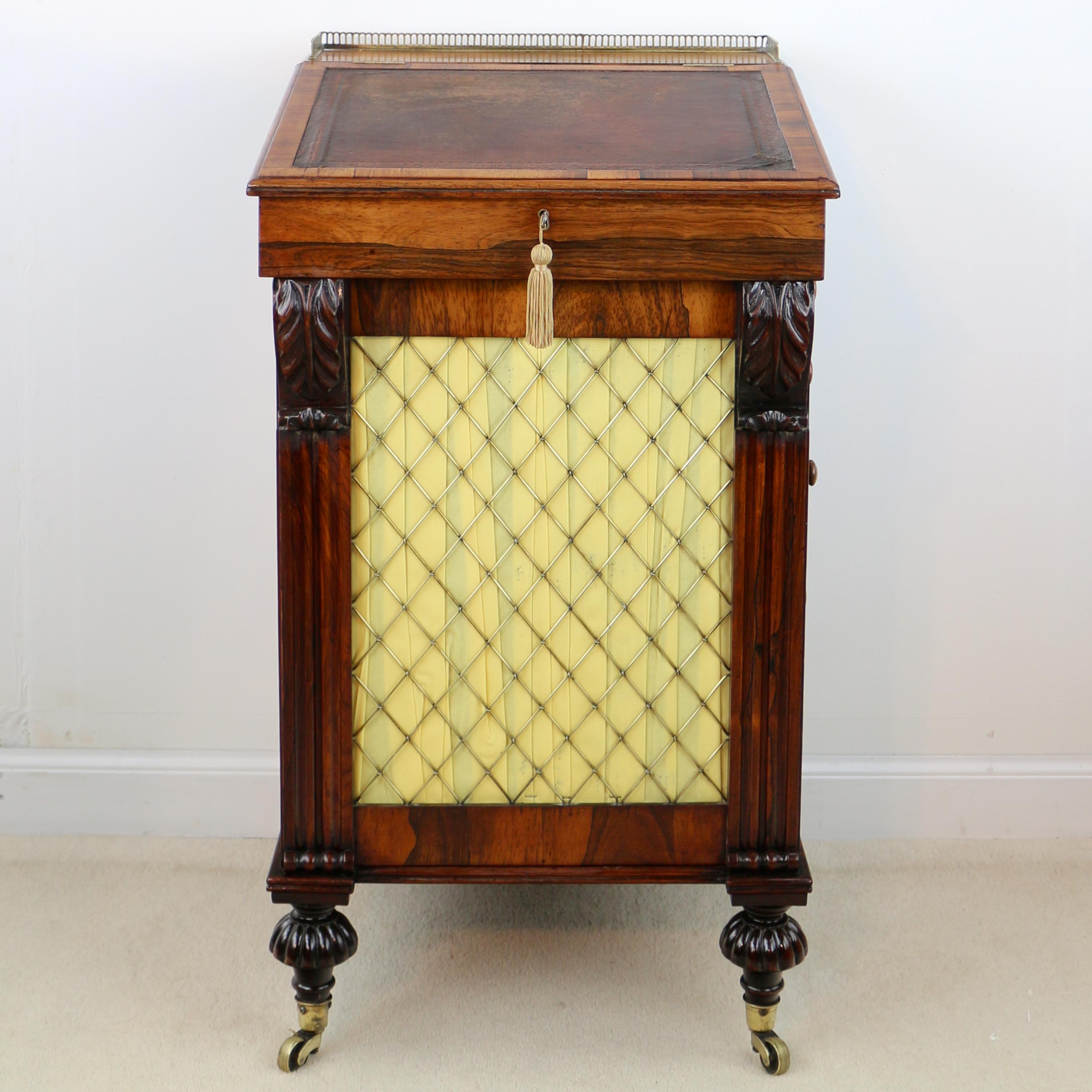 A super Regency rosewood Davenport dating to circa 1820 and featuring a rare brass grille front flanked by acanthus carved corbels and fluted pilasters. The sliding top with a pierced brass gallery and pen drawer above a black and gilt tooled