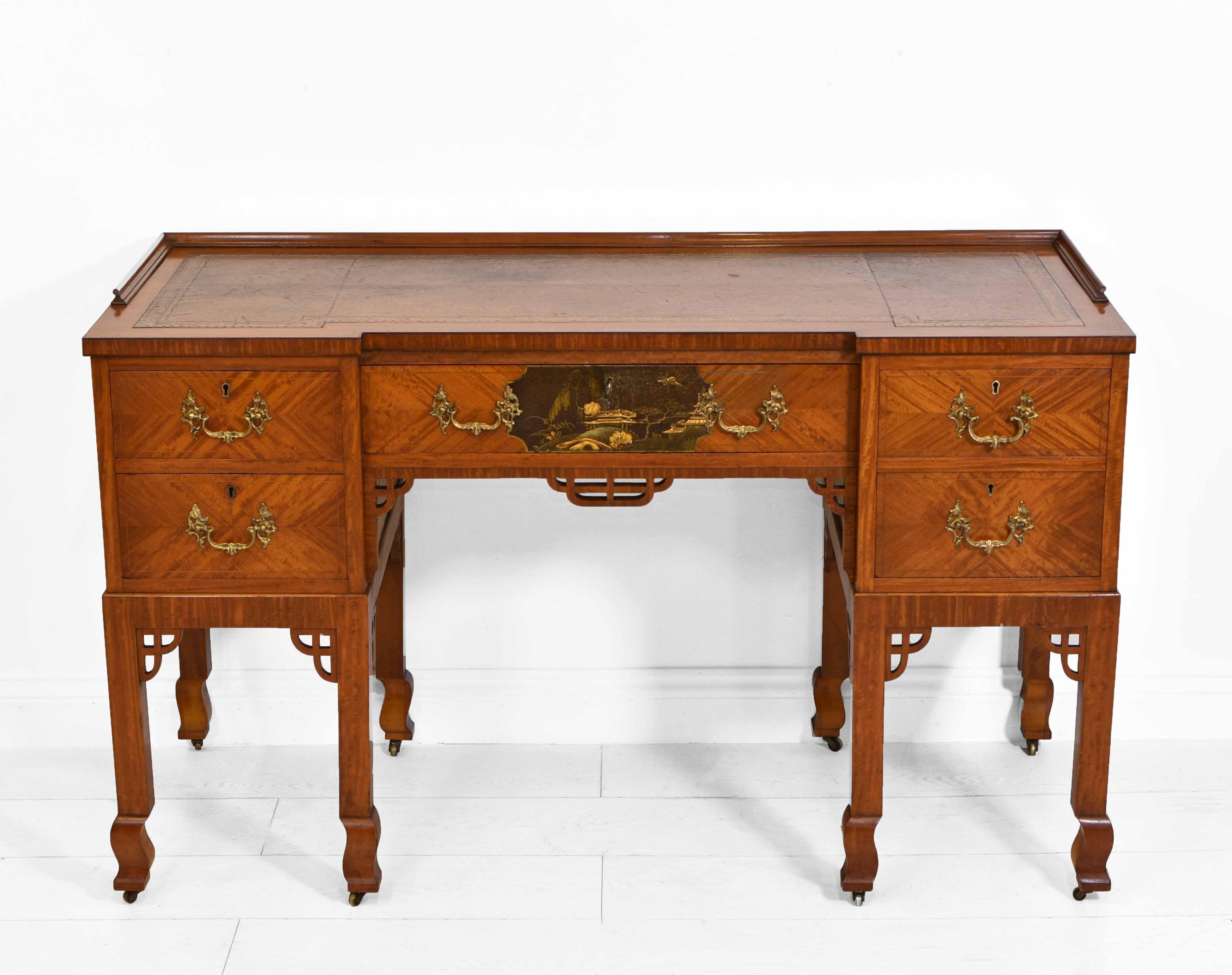 An antique Edwardian Japanese manner satinwood inverted breakfront desk, with leather and gilt tooled inset. English. Circa 1900.

This good quality desk has a small Japanned landscape scene to the central drawer, along with ornate gilt brass