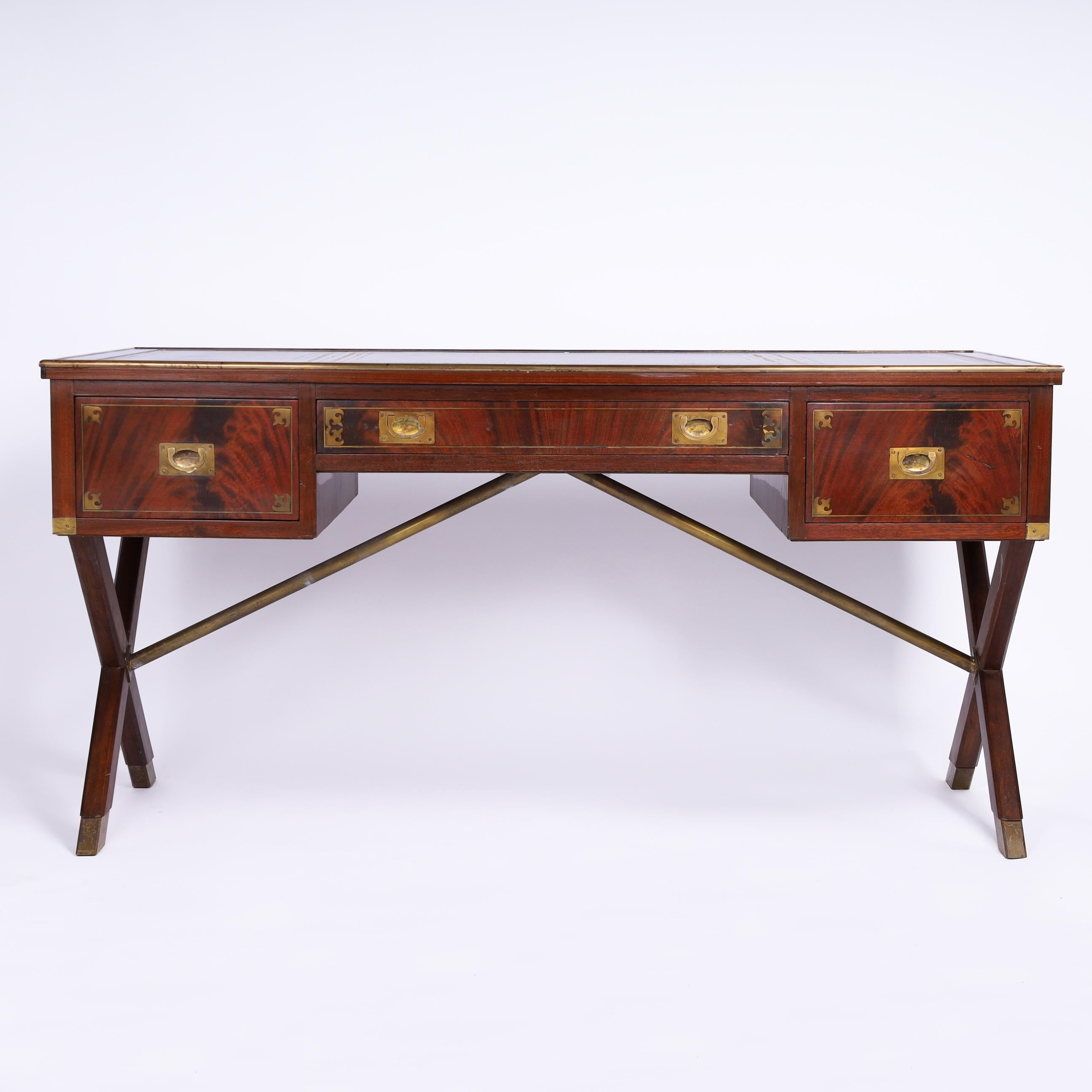 Handsome antique English desk crafted in mahogany, featuring the original three tooled leather panels on top, brass campaign hardware, three drawers with inlaid borders in front and faux drawers on the reverse and X style legs with brass stretcher