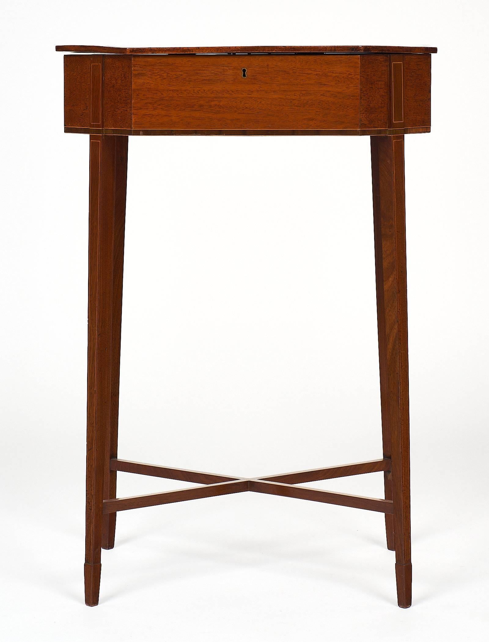 English antique sewing table made of mahogany. This piece has a cross banding border on the rectangular hinge top with clipped corners, and tulip wood stringing on the four square, tapered legs. The legs are supported by an X-stretcher. This piece