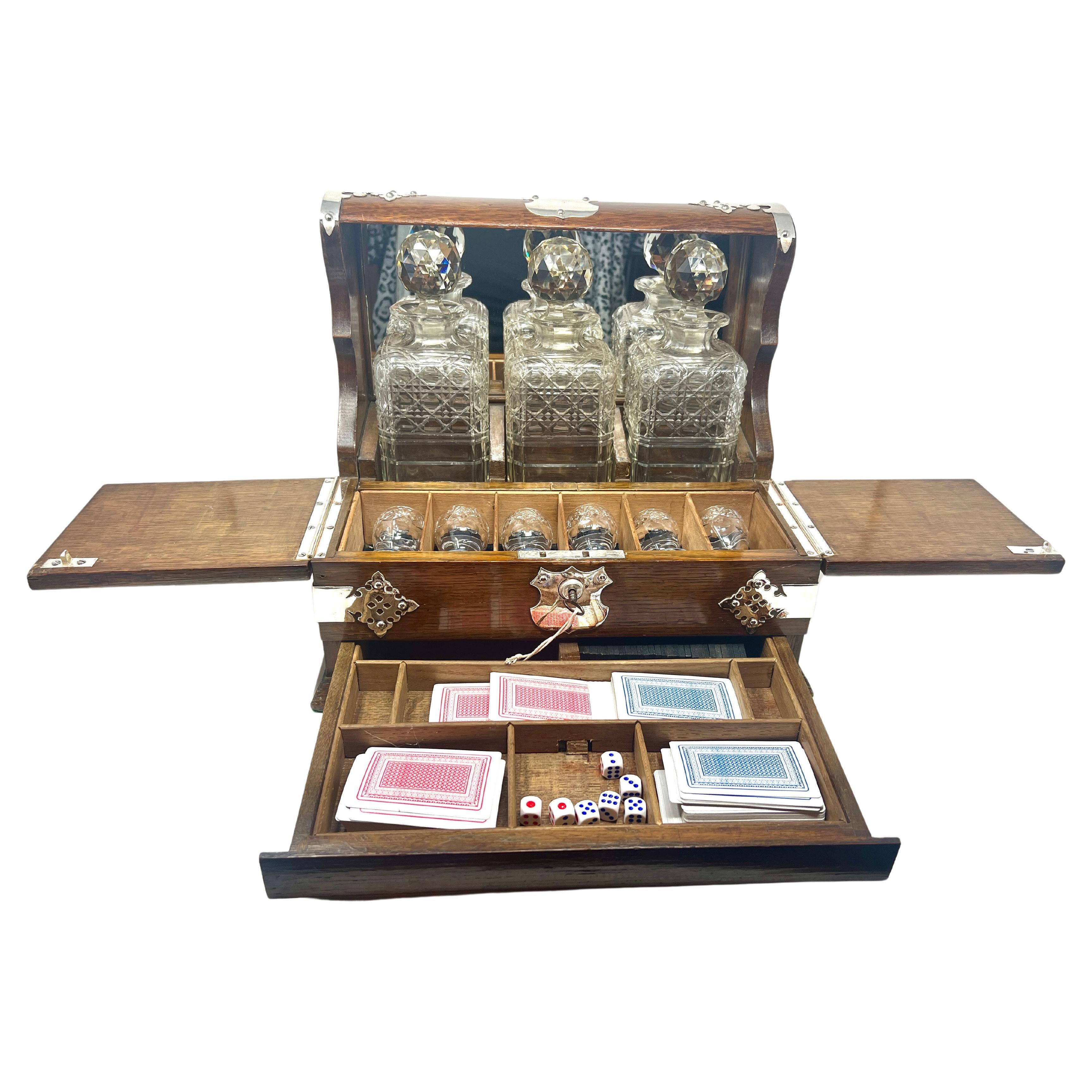 Antique English Sheffield Silver Mounted Golden Oak and Cut Crystal Games Box Tantalus with Fitted Interior and Mirrored Back, Circa 1890's.
Fitted Interior Includes 3 Crystal Decanters, 6 Crystal Cordials, Playing Cards & Dice.