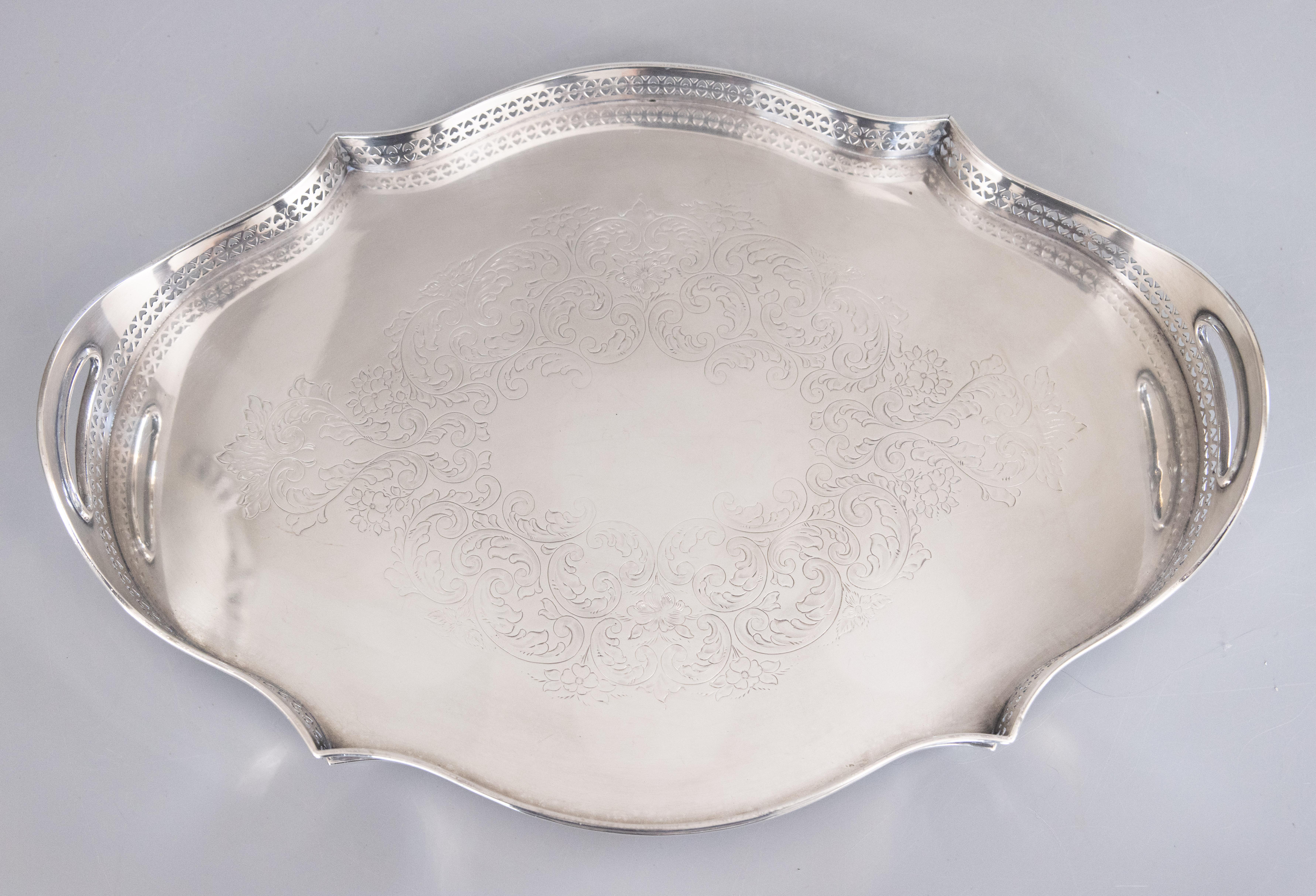 A lovely antique English silverplate serpentine gallery serving or barware tray. Hallmarks on reverse. This gorgeous tray is decorated with elaborate chasing, a lovely scalloped design, pierced gallery, and charming bun feet, perfect for serving or