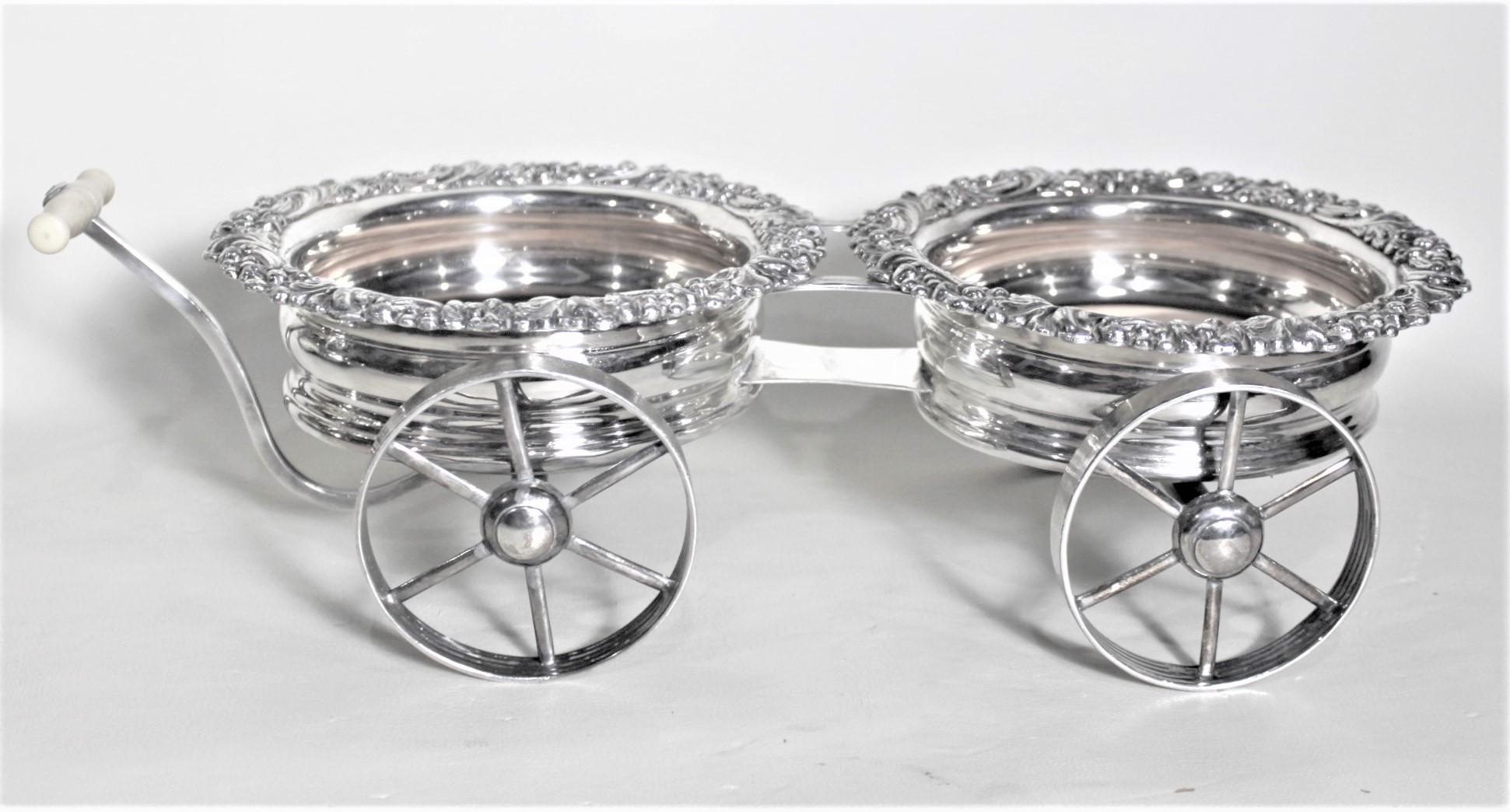 This Sheffield plated figural wine coaster wagon is unsigned but presumed to have been made in England in circa 1890 in the period Victorian style. The wagon features two silver plated wine bottle coasters with leaf and berry decorated rims and