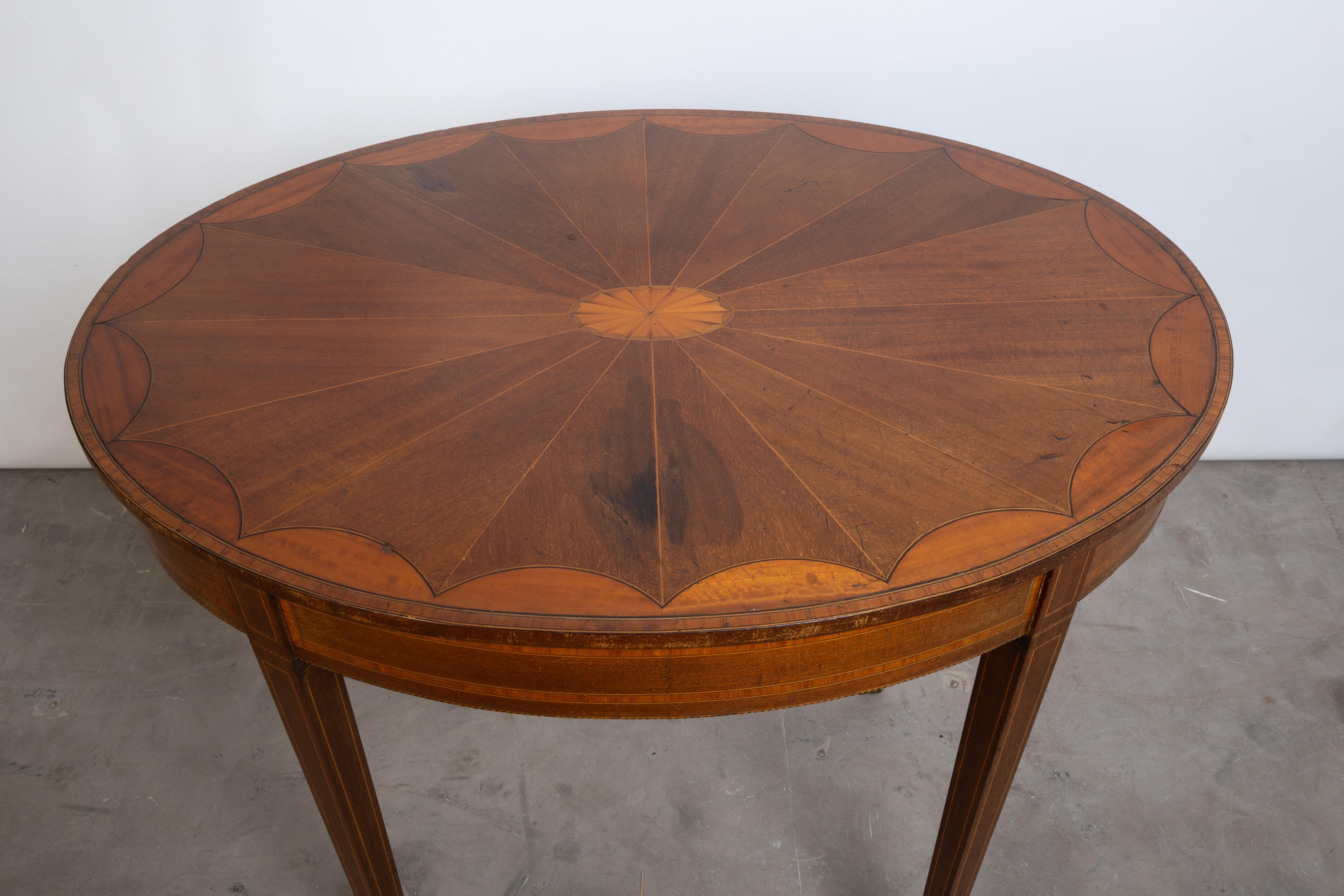 Ancienne table centrale ovale marquetée de style Sheraton Revival anglais, vers 1900

Marqueterie en éventail réalisée à partir d'un mélange de placages dont l'acajou et le bois de satin. Baguettes croisées en buis et cordes en ébène. Elle repose