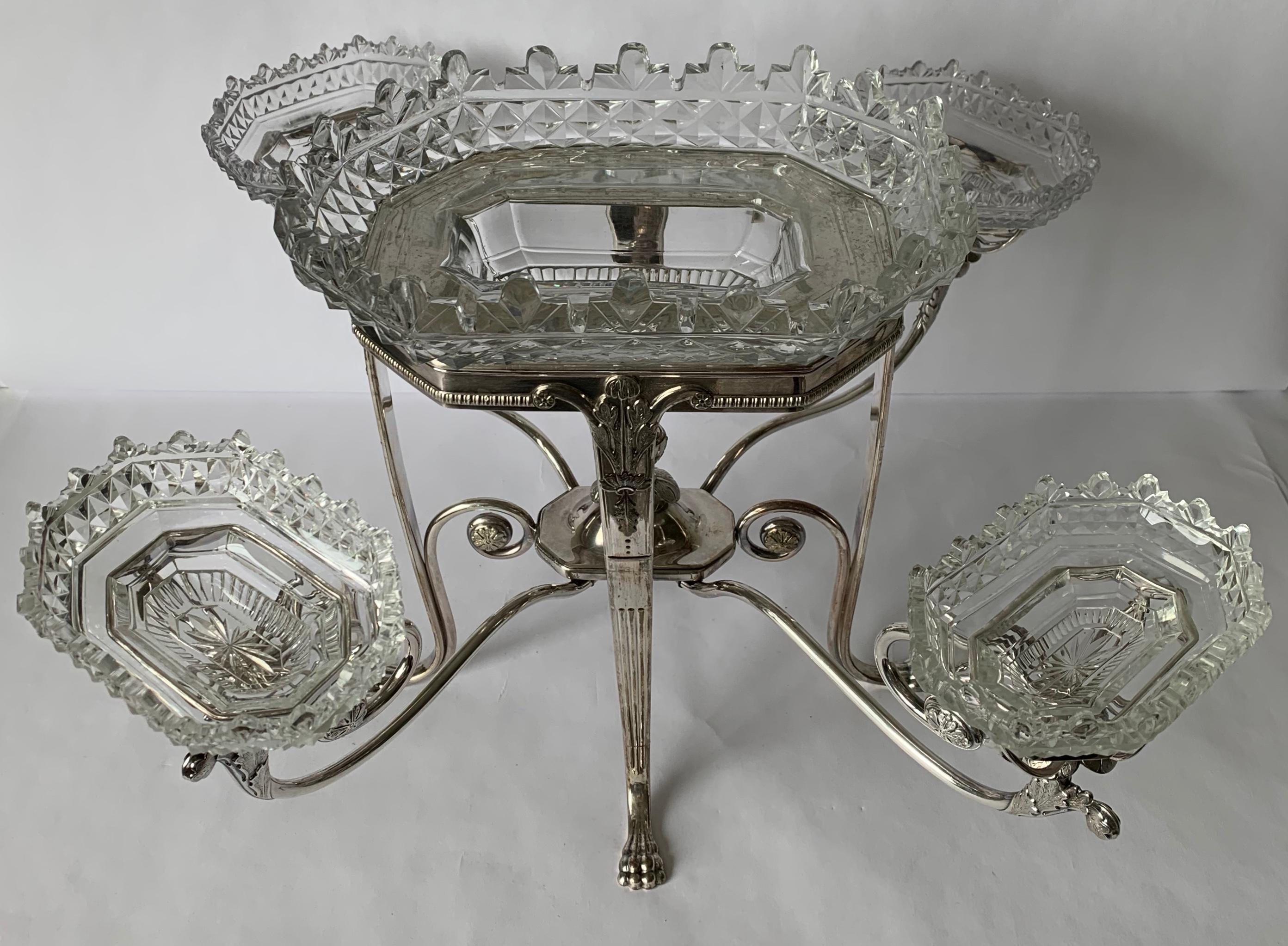 Antique English silver plated epergne. Four arm design, each with cut glass inset bowl. Center cut glass inset bowl. Stand alone is 10” tall x 5.5” deep x 8.25” wide. Stamped on the underside.