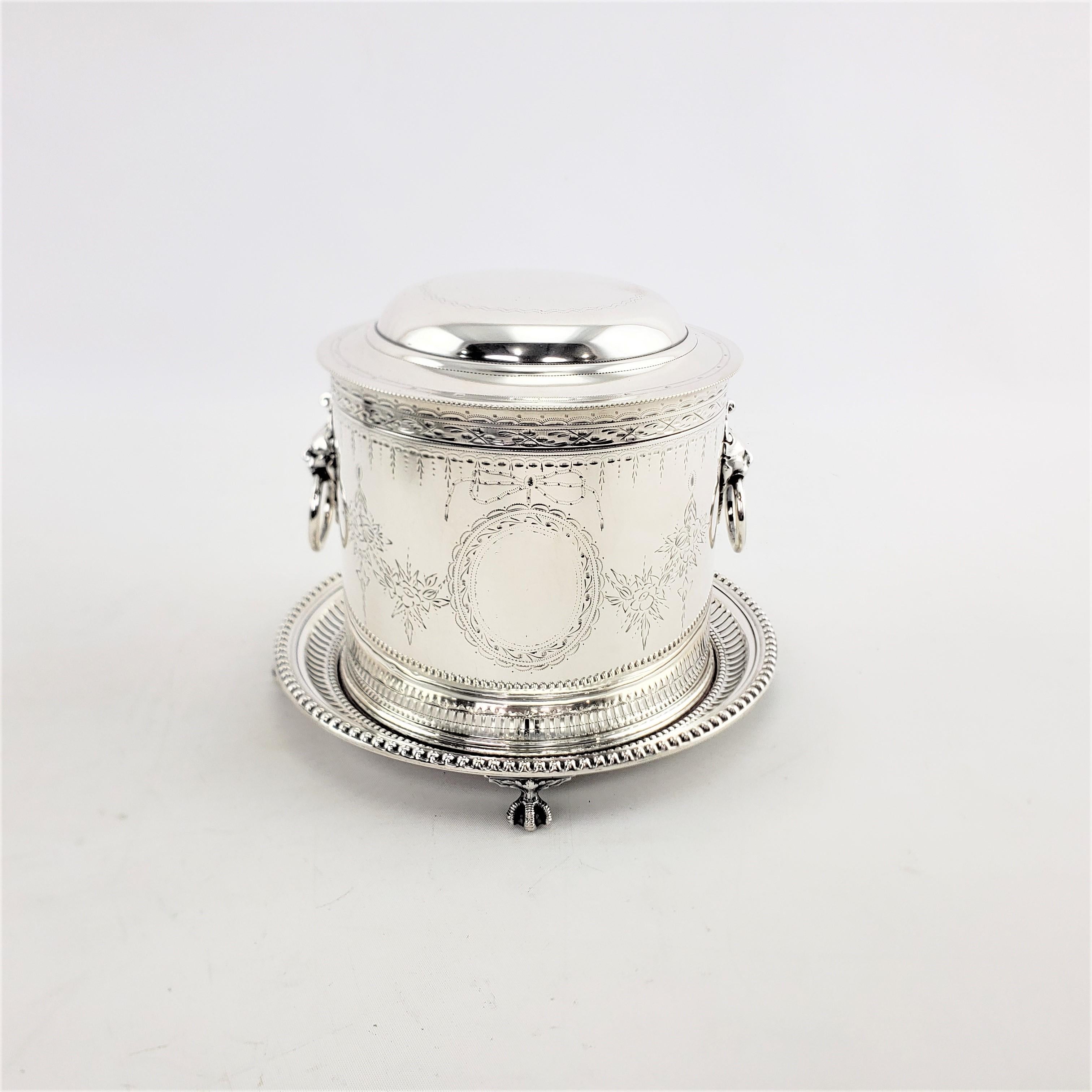 This silver plated biscuit barrel is hallmarked by an unknown maker, and originates from England and dating to approximately 1910 and done in the period Edwardian style. This biscuit barrel has a hinged lid with ornately cast lion mounted handles on
