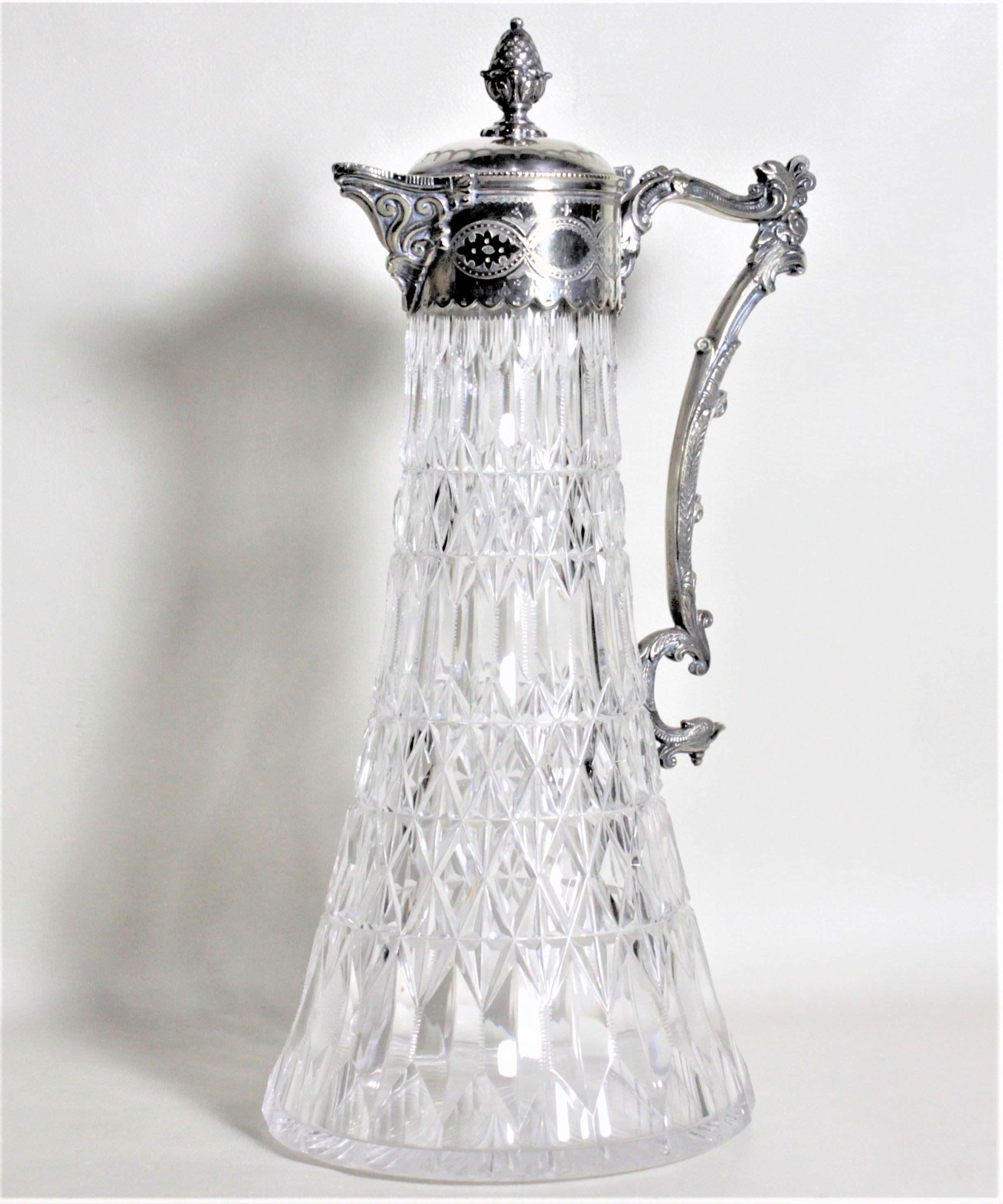 This antique silver plate and cut crystal claret jug was most likely made in England in circa 1900 in the Victorian style. The jug features a pineapple finial on the raised lid and engraved intertwined medallions using a greenery motif and raised