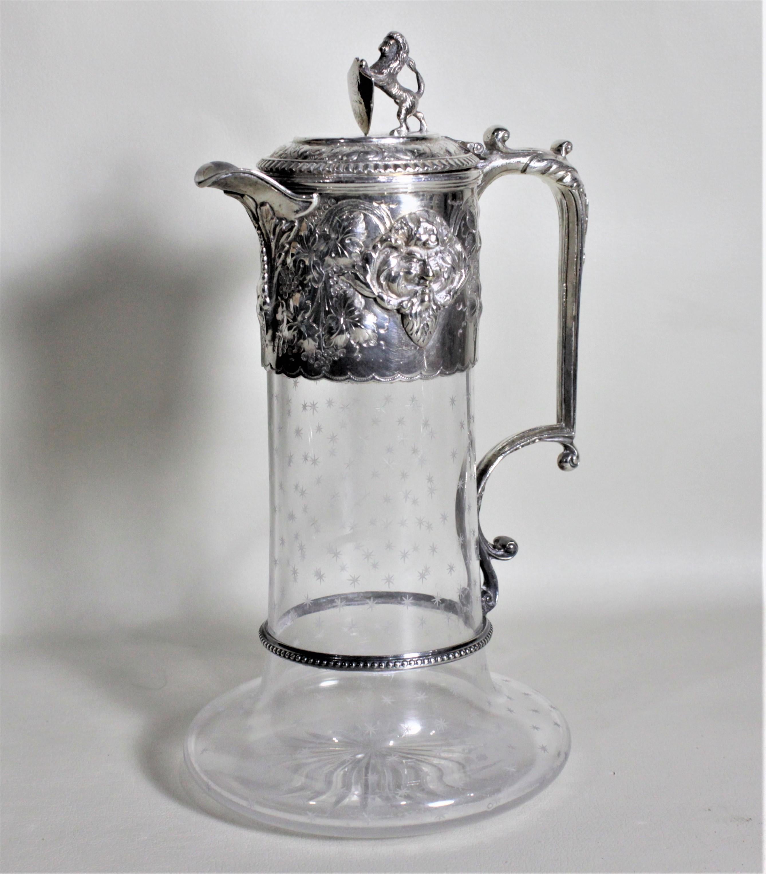 This antique silver plate and cut crystal claret jug was most likely made in England in circa 1900 in the Victorian style. The jug features a standing figural lion holding a shield on the lid and an ornate raised flower and leaf design motif