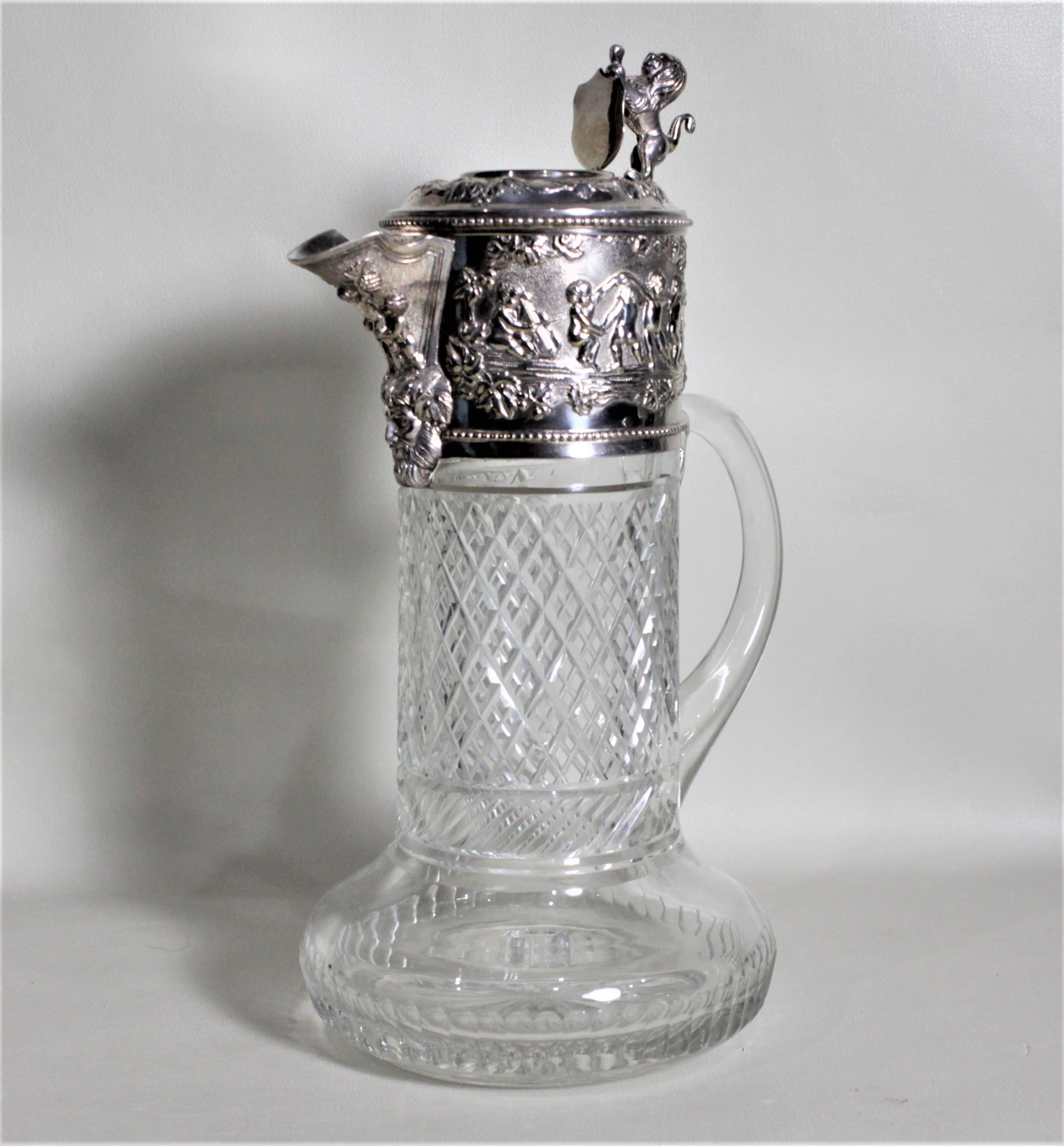 This antique silver plate and cut glass claret jug was most likely made in England in circa 1900 in the Victorian style. The jug features a rearing figural lion finial on the lid and a very ornate raised cherub motif decoration on the wide banding