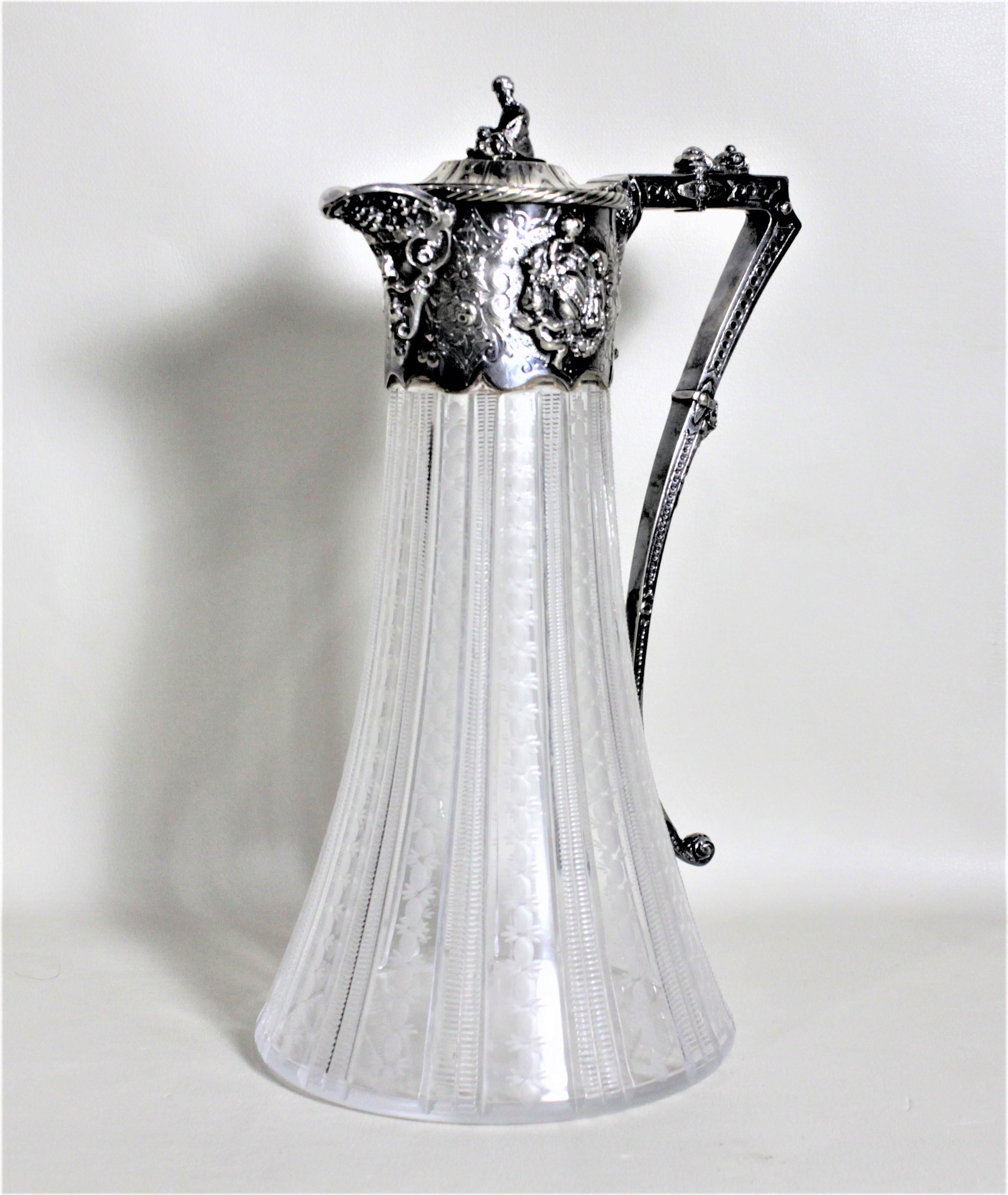 Esta antigua jarra de clarete de chapa de plata y cristal tallado se fabricó probablemente en Inglaterra hacia 1900, en estilo victoriano. La jarra presenta un remate figurado sentado en la parte superior de la tapa y una decoración ornamentada con