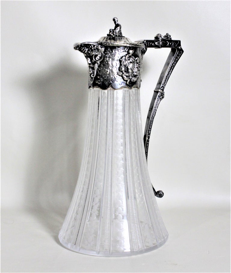 This antique silver plate and cut glass claret jug was most likely made in England in circa 1900 in the Victorian style. The jug features a seated figural finial on the top of the lid and ornate raised shield motif decoration on either side of the
