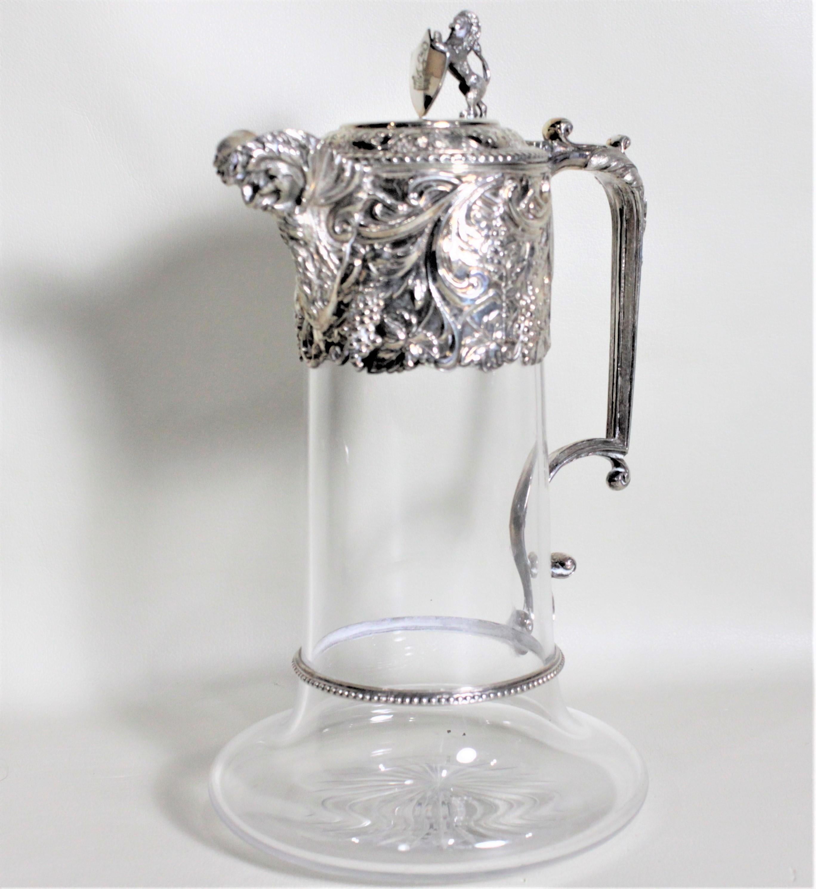This antique silver plate and cut glass claret jug was most likely made in England in circa 1900 in the Victorian style. The jug features a figural standing lion holding a shield on the top of the ornately decorated raised top with very pronounced