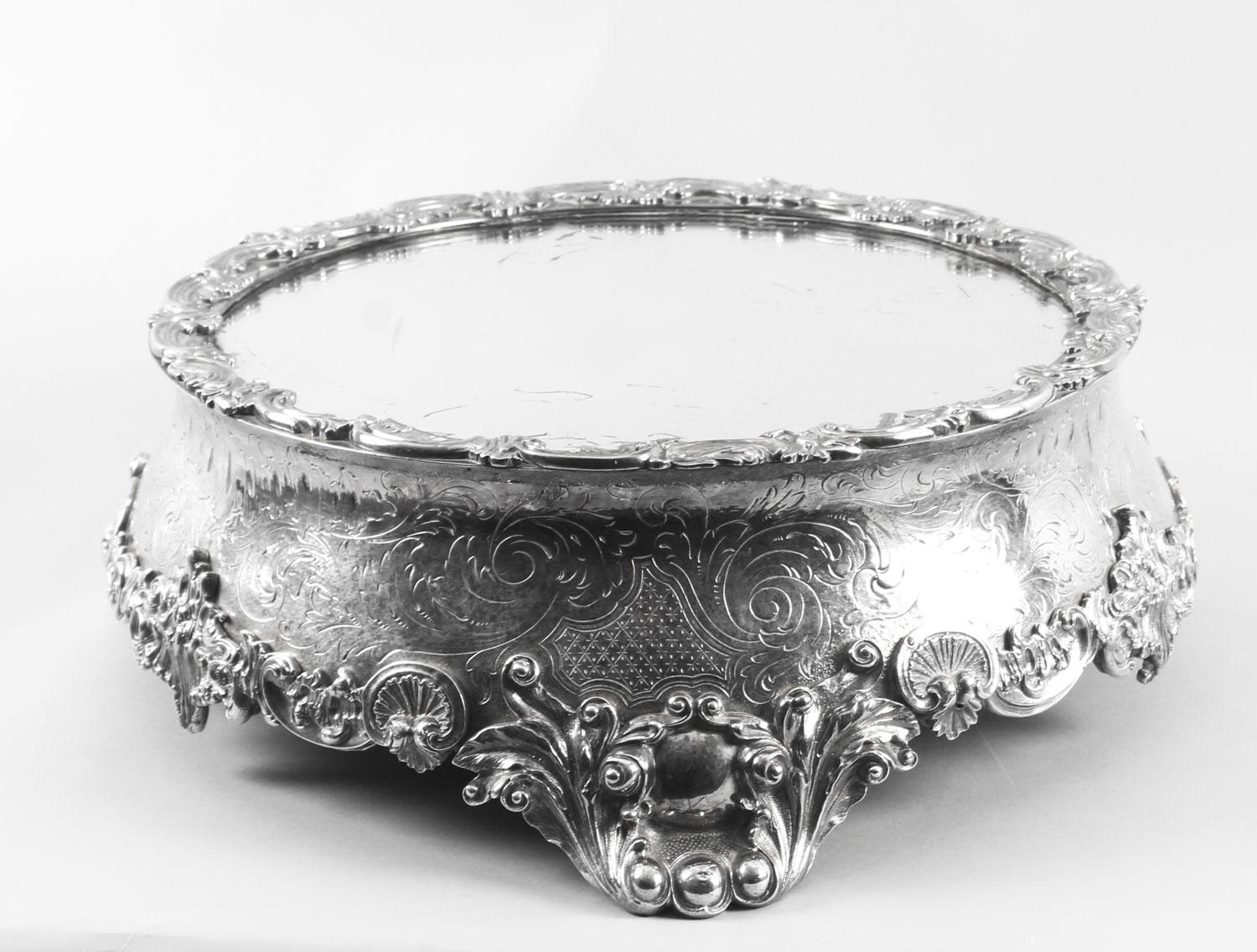 This is a fabulous antique Victorian silver plated cake stand with the original mirrored plate within a foliate and scroll cast border above a cylindrical frieze with engraved decoration and raised on three foliate scroll cast bracket feet, circa