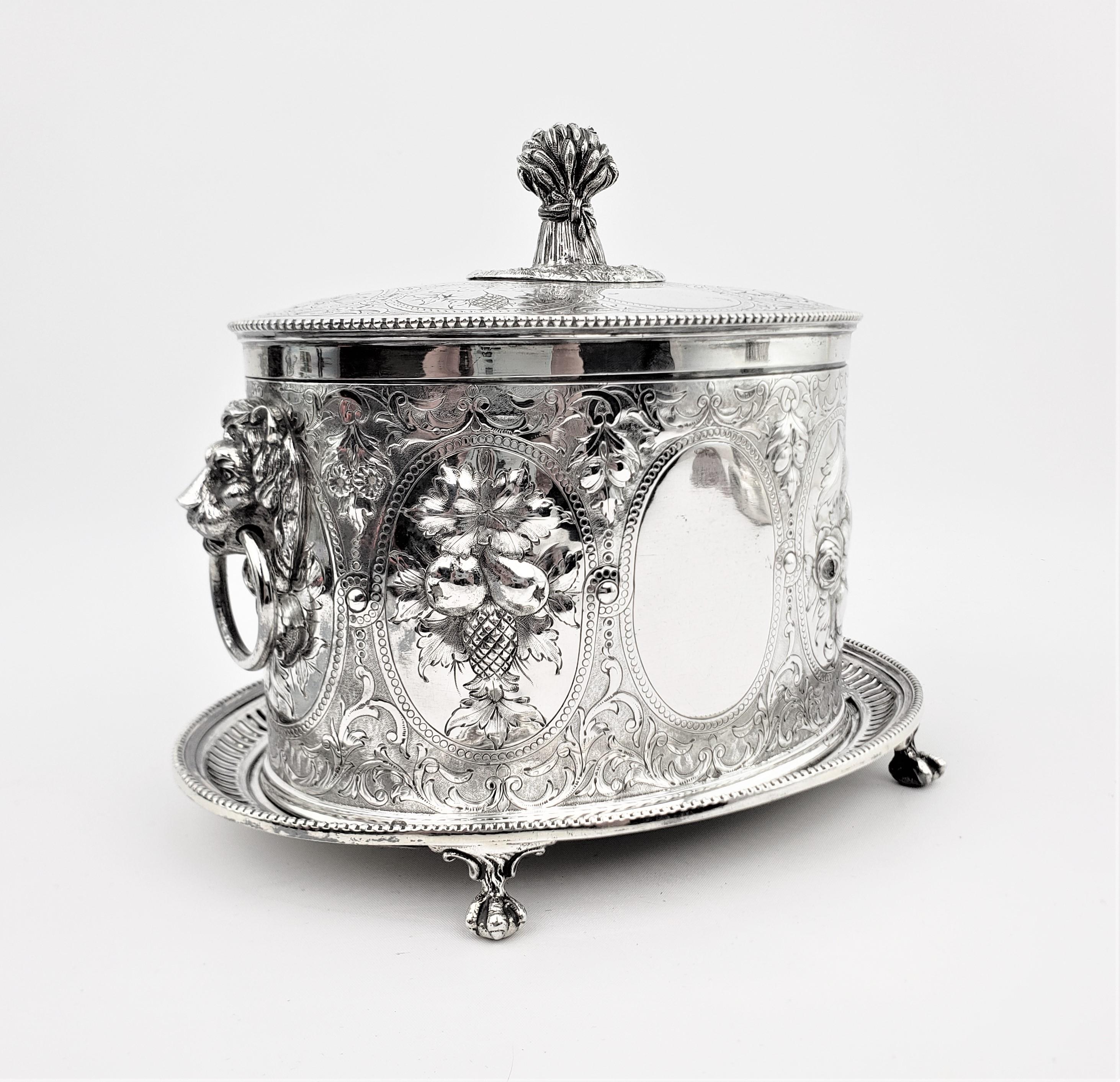 This antique oval shaped and silver plated biscuit barrel was made in England in approximately 1880 in a period Victorian style. This biscuit barrel has a central shield on both the front and back, which is surrounded by a harvest themed decoration