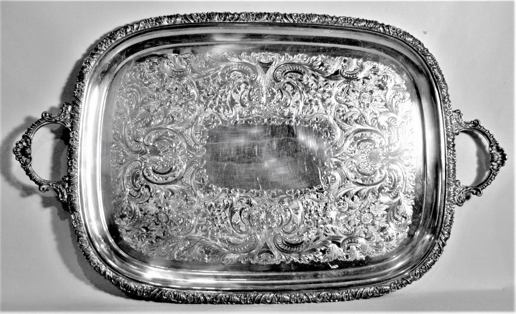 This ornate silver plated serving tray was made in England in approximately 1950 in a Victorian style. The tray has ornately decorated handles and outer rim done with a scrolling floral motif, which is accented by the scrolled leaves engraved on the