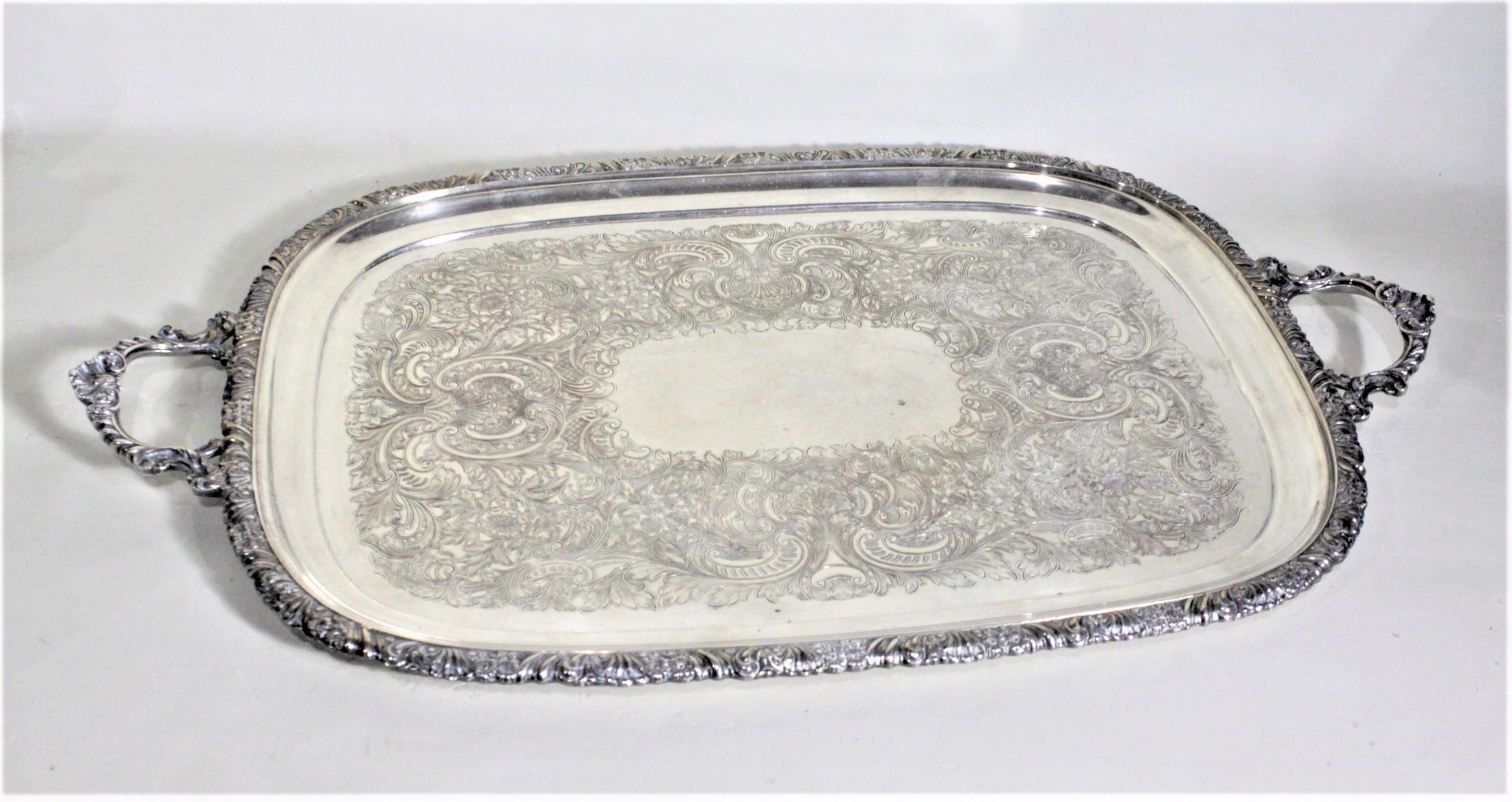 This ornate silver plated serving tray was made in England in approximately 1920 in a Victorian style. The tray has ornately decorated handles and outer rim done with a scrolling floral motif, which is accented by the scrolled leaves engraved on the