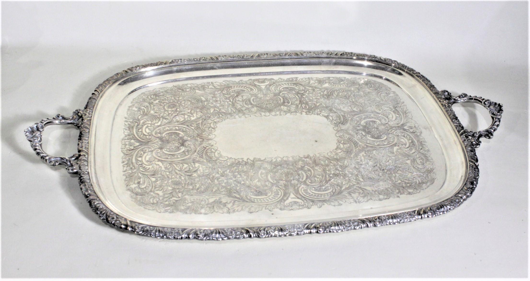 Esta ornamentada bandeja de servir bañada en plata se fabricó en Inglaterra aproximadamente en 1920, en estilo victoriano. La bandeja tiene las asas y el borde exterior ornamentados con un motivo floral en volutas, que se acentúa con las hojas en