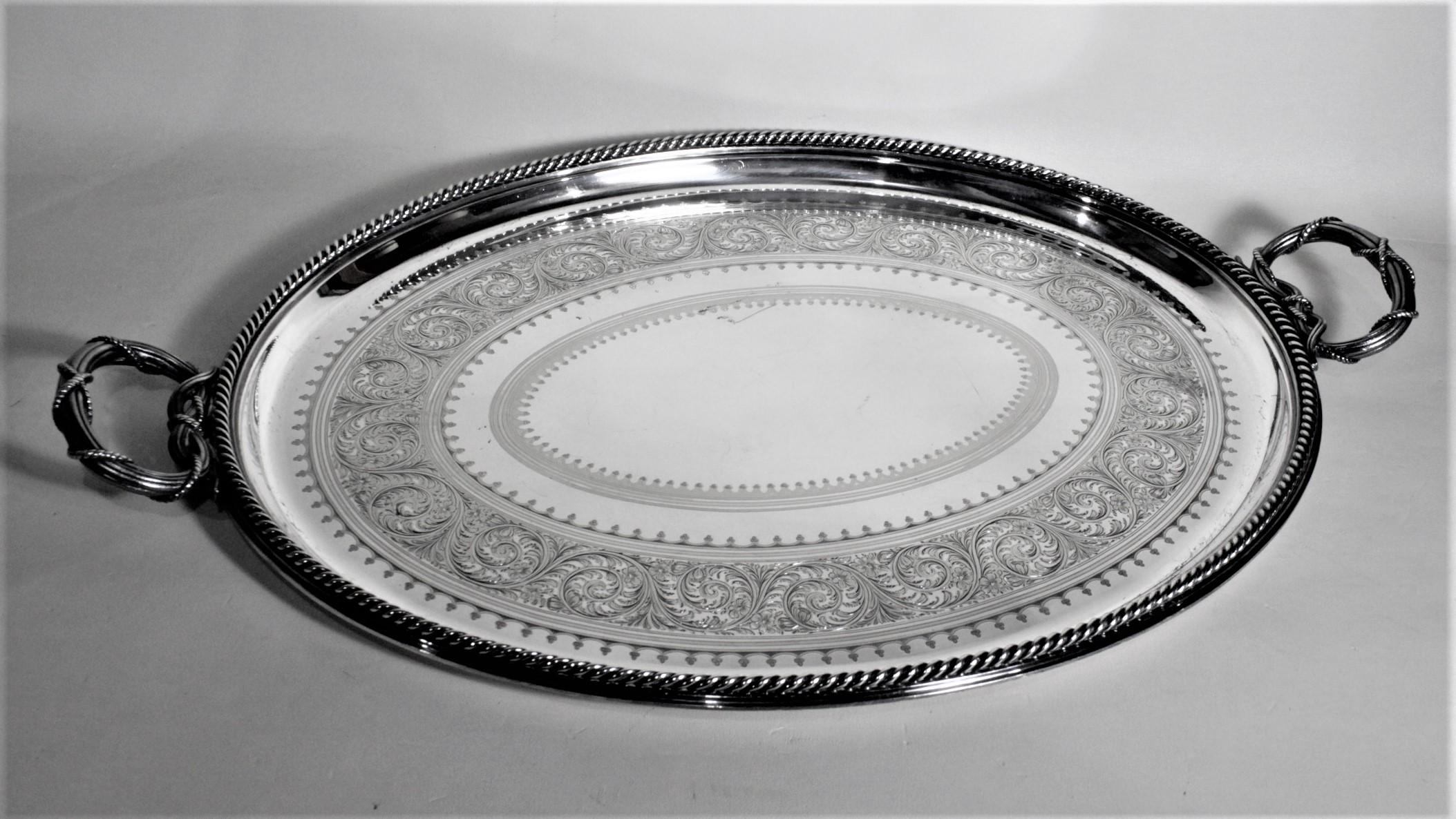 This antique silver plated serving tray was made by the Elkington & Co. of England in circa 1890 in the period Victorian style. The tray has a nicely engraved outer band with a swirled floral motif and two smaller bands of a rope or garland which