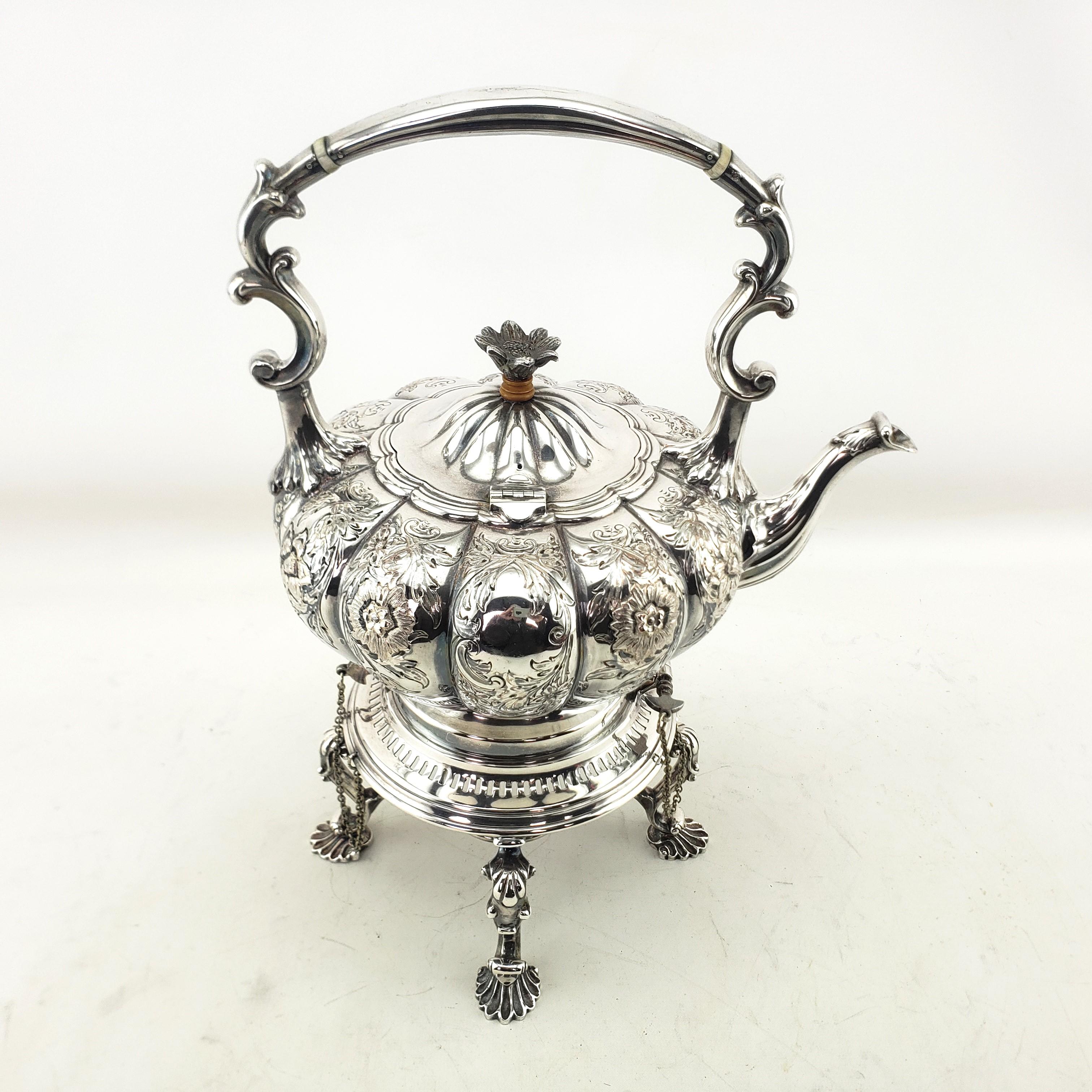 This antique hot water tipping kettle is unsigned by a maker, but originated from England and dates to approximately 1900 and done in an Art Nouveau style. The kettle and stand are done in silver plate with metal chains and pins. The kettle is