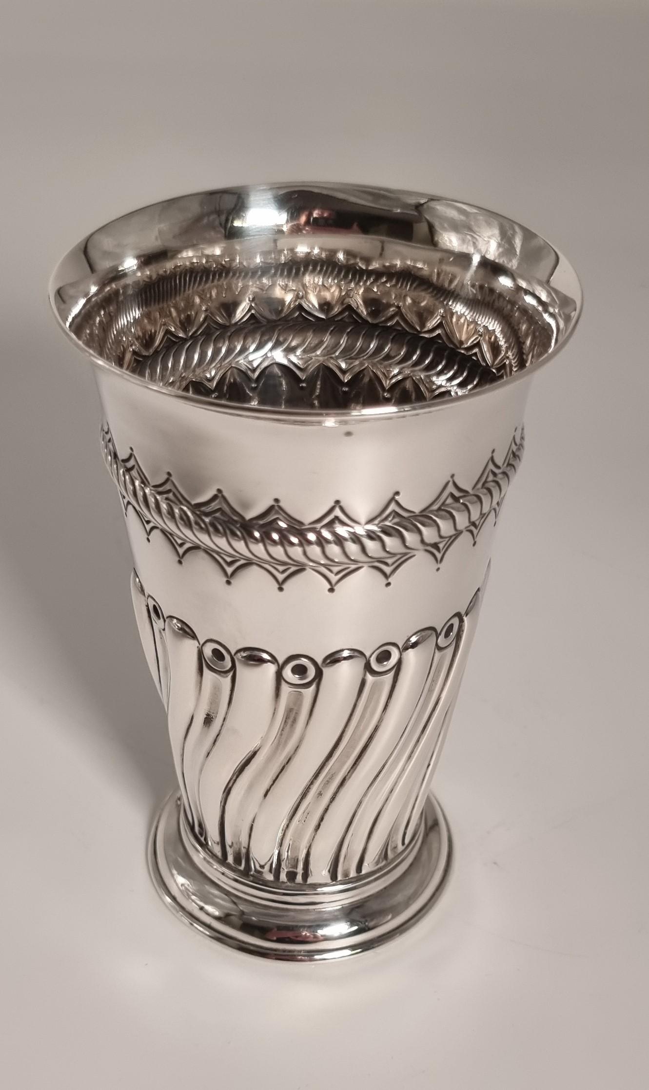 Questo vaso d'argento massiccio molto appariscente poggia su un piede rialzato modellato e a cupola. Il corpo alto e slanciato si svasa lentamente fino ad arrivare a un bordo semplice e ampio.

La parte inferiore del corpo è decorata con un motivo